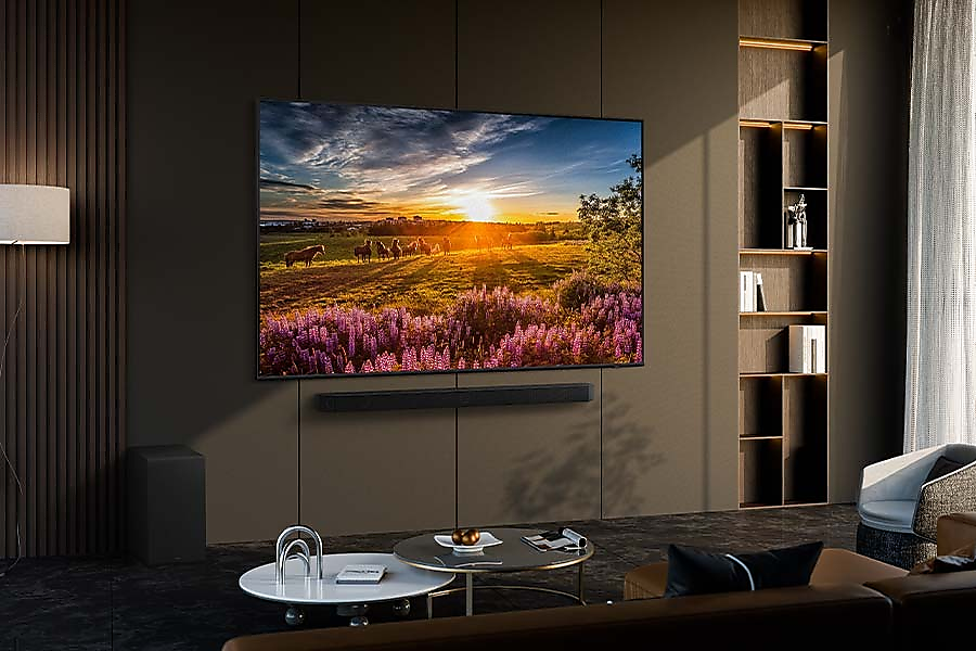 TV naplementét jelenít meg egy mező felett. Soundbar a TV alatt. Fekete bútorok. Sötét fal.