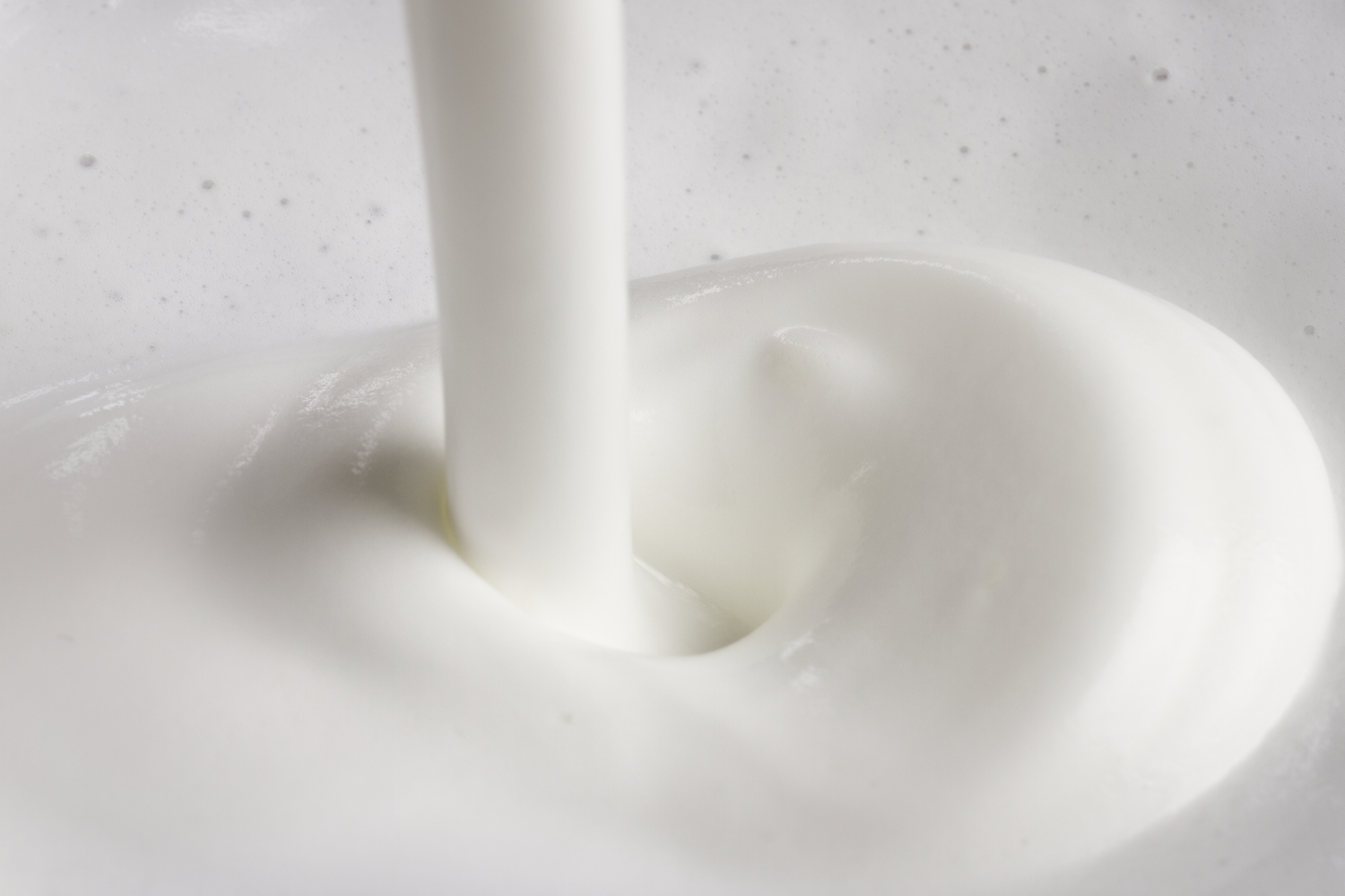 Nahaufnahme von Milch, die gießt und einen Wirbel erzeugt, vor weißem Hintergrund.