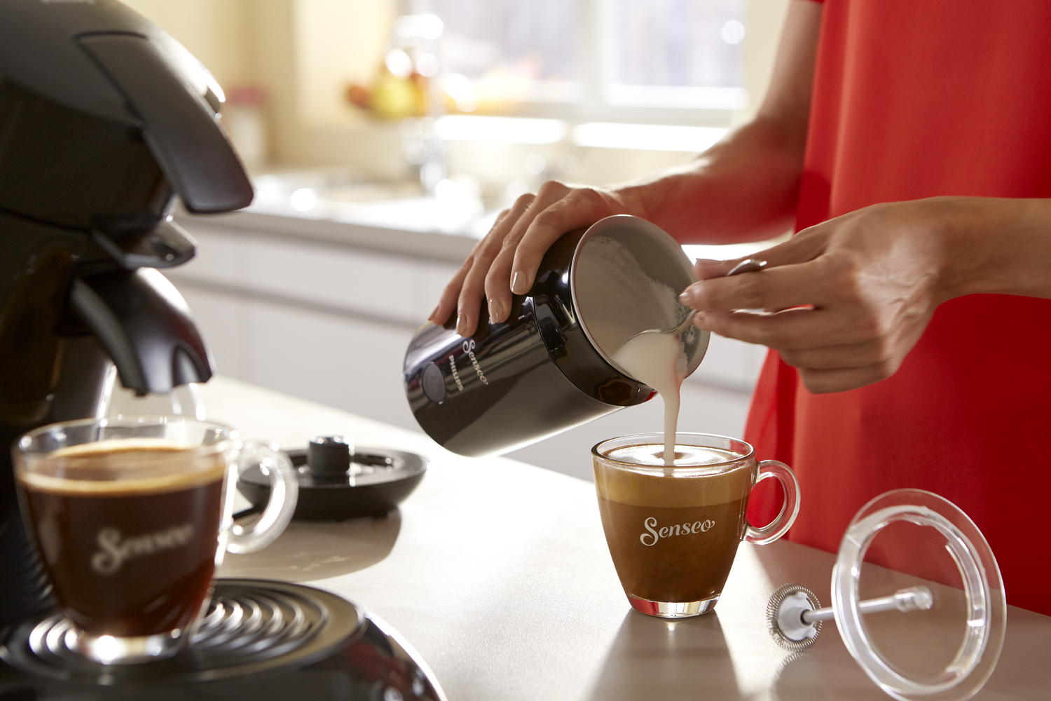 Person gießt Milch aus einem schwarzen Behälter in eine gläserne Tasse.