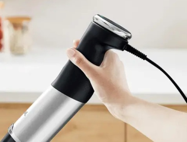 Dłoń trzymająca czarno-srebrny blender ręczny z czarnym przewodem zasilającym.