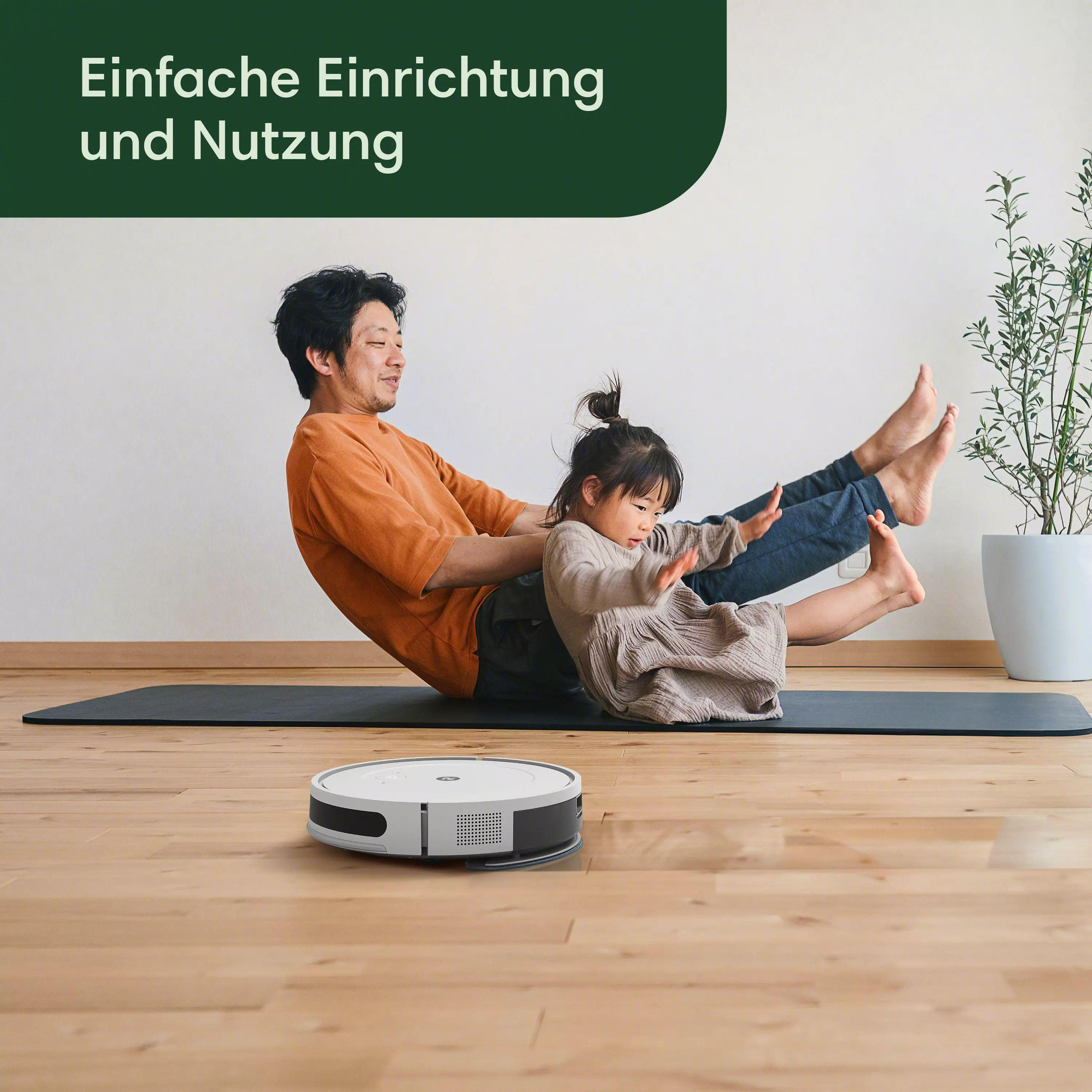 Ein Mann und ein Kind sitzen auf dem Boden neben einem Roboter-Staubsauger.