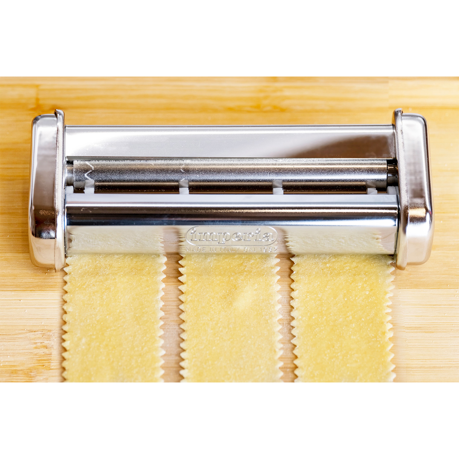 Macchina per la pasta con tre strisce di pasta fresca su un tagliere di legno.