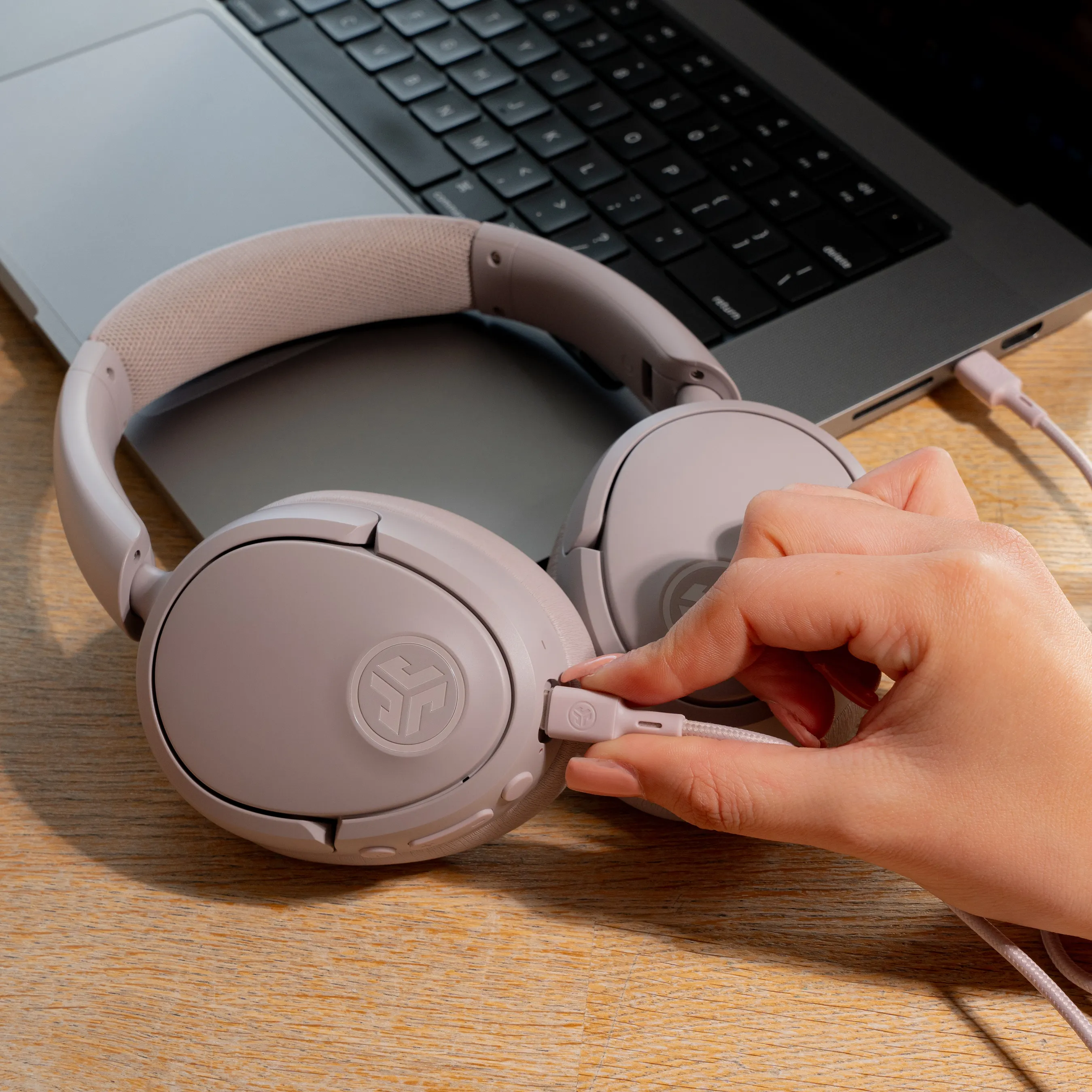 Eine Person, die ein rosa USB-C-Kabel in ein hellrosa Kopfhörerpaar steckt.