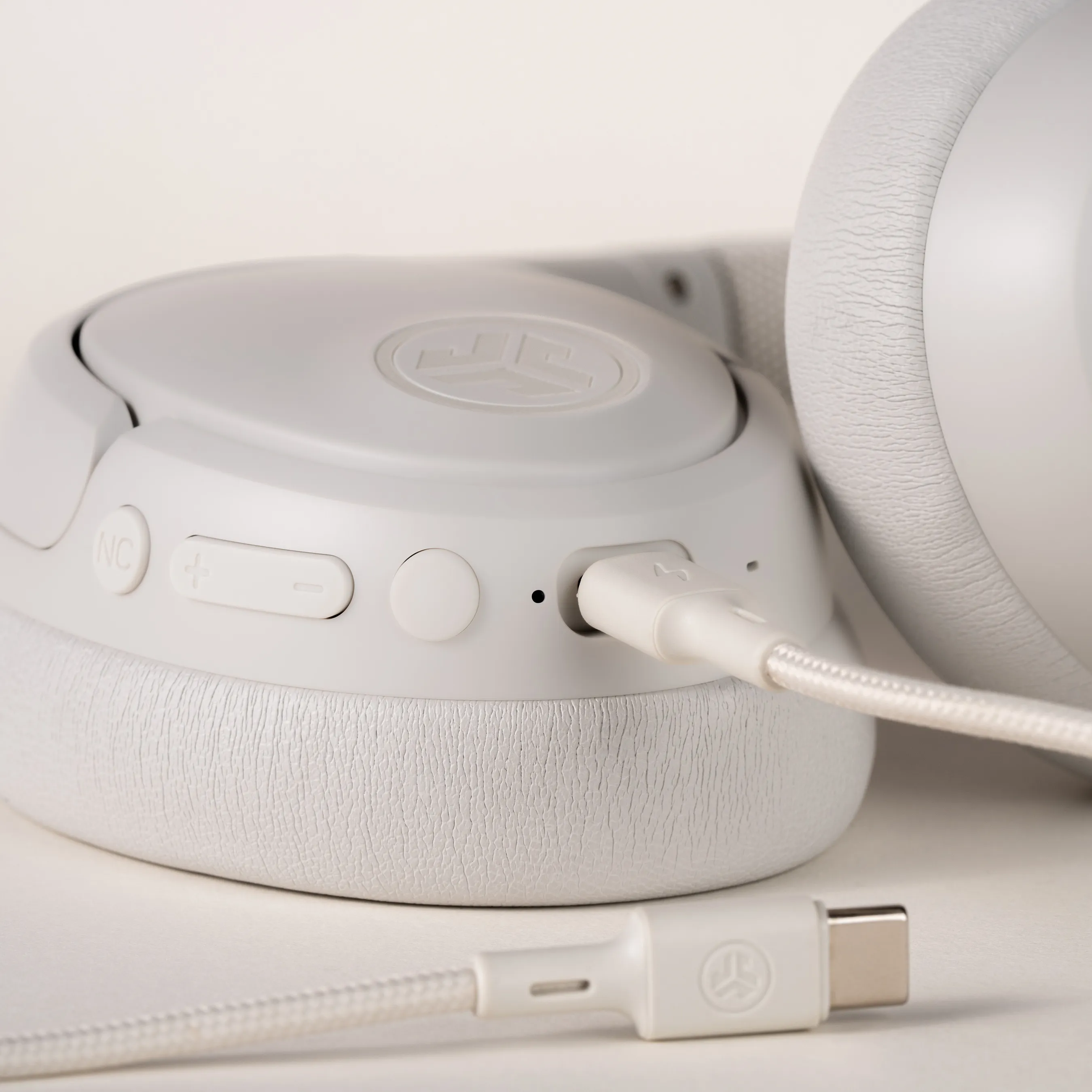 Weiße Kopfhörer mit weißem USB-C-Kabel, das eingesteckt ist, auf weißer Oberfläche.
