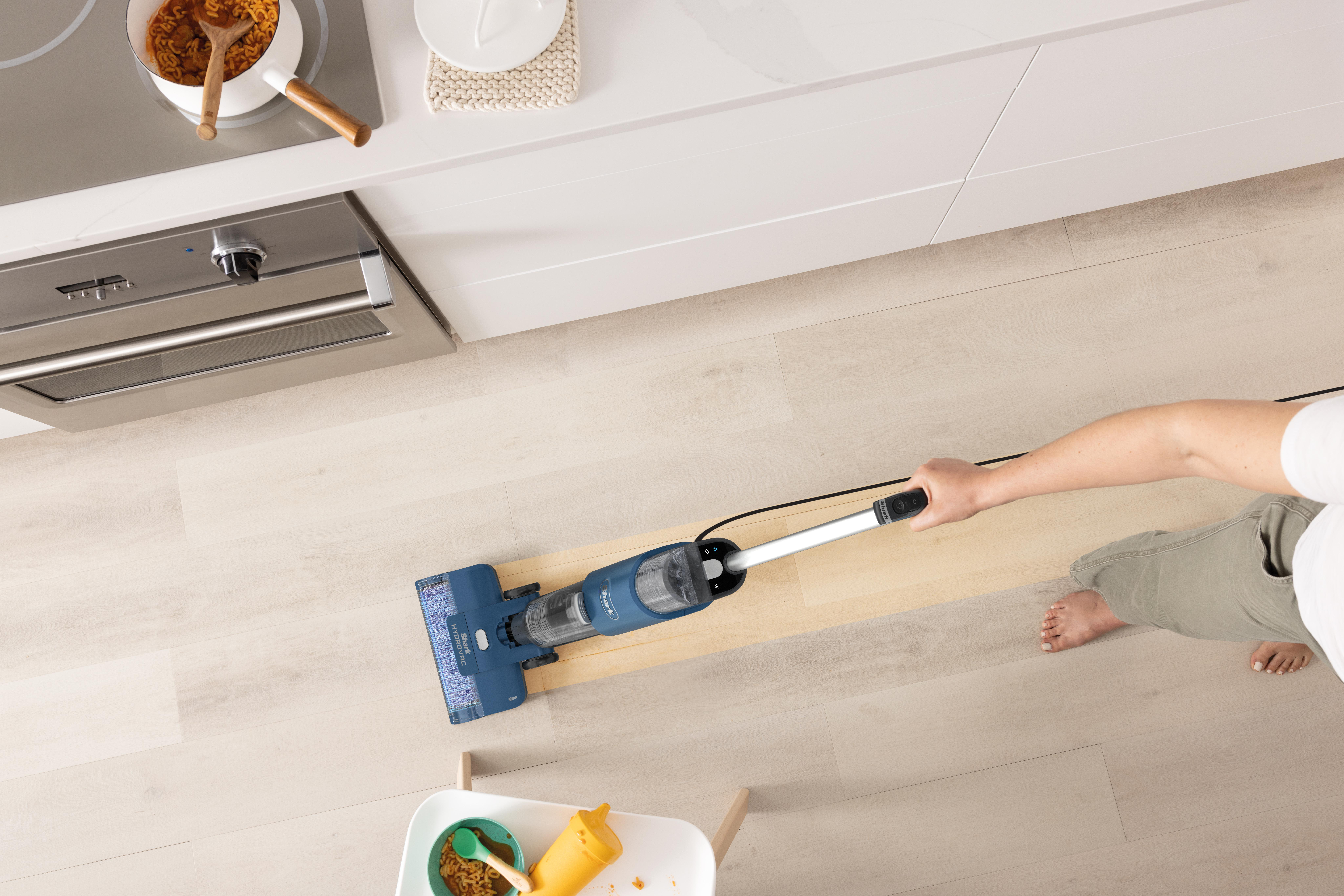 Person saugt einen Holzboden mit einem aufrechten Staubsauger.