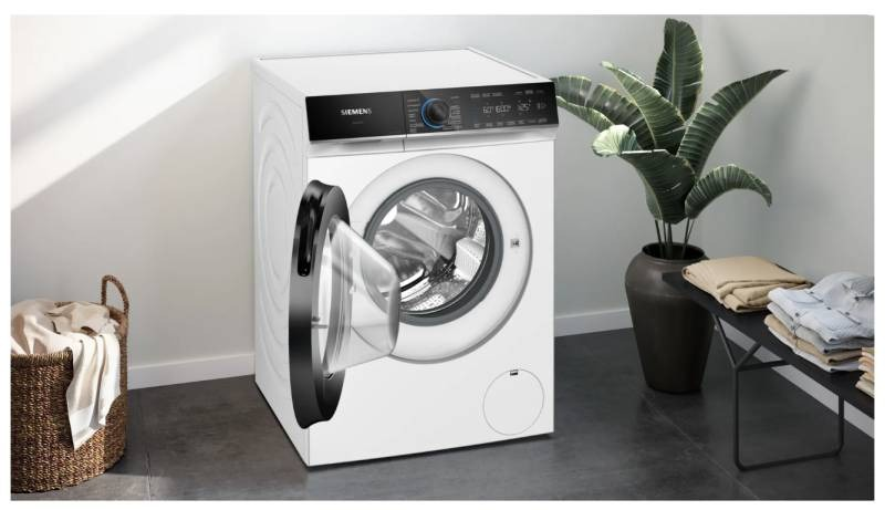 Lave-linge blanc avec la porte ouverte, avec un panier et une plante en arrière-plan.