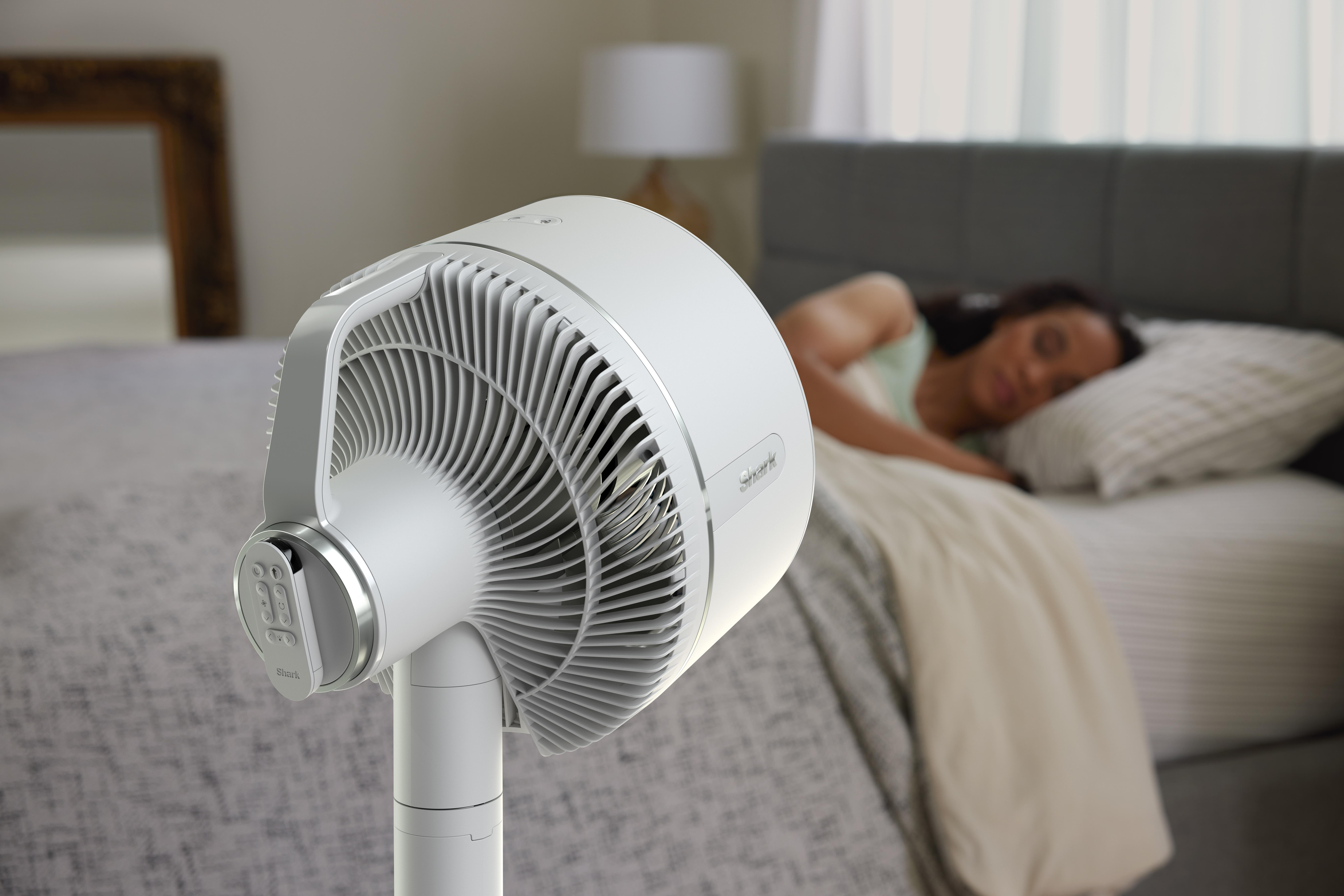 Weißer Ventilator mit silbernen Akzenten, eine schlafende Frau im Hintergrund.