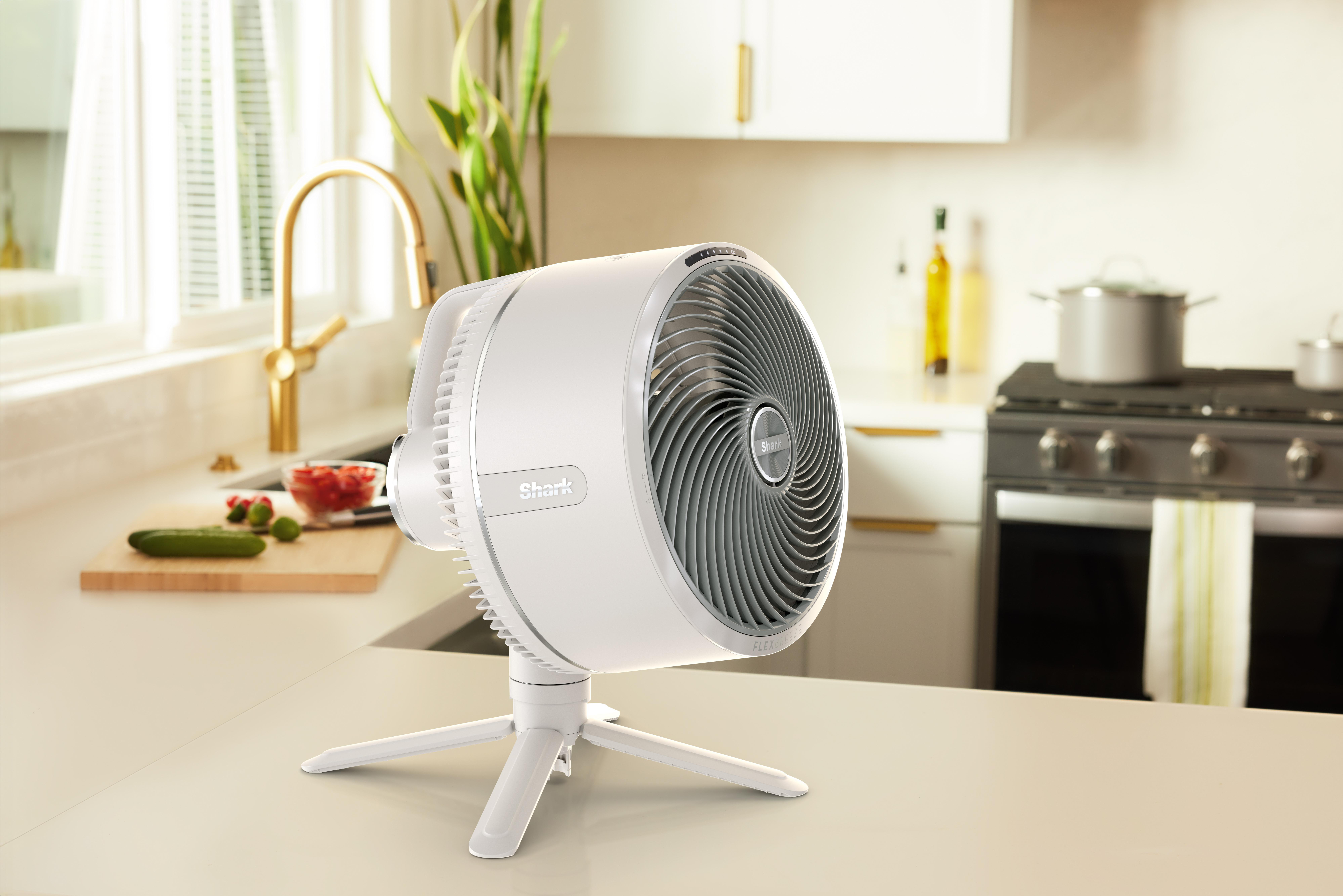 Ein weißer Ventilator auf einem weißen Ständer, auf einer Arbeitsplatte in einer Küche.