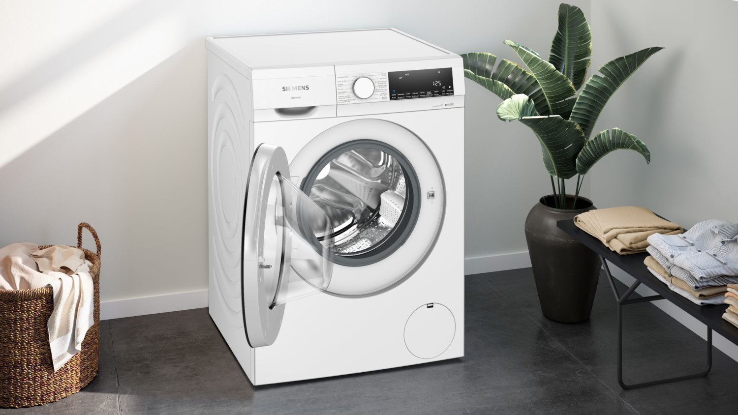 Un lave-linge blanc avec une porte ouverte et une plante en arrière-plan.