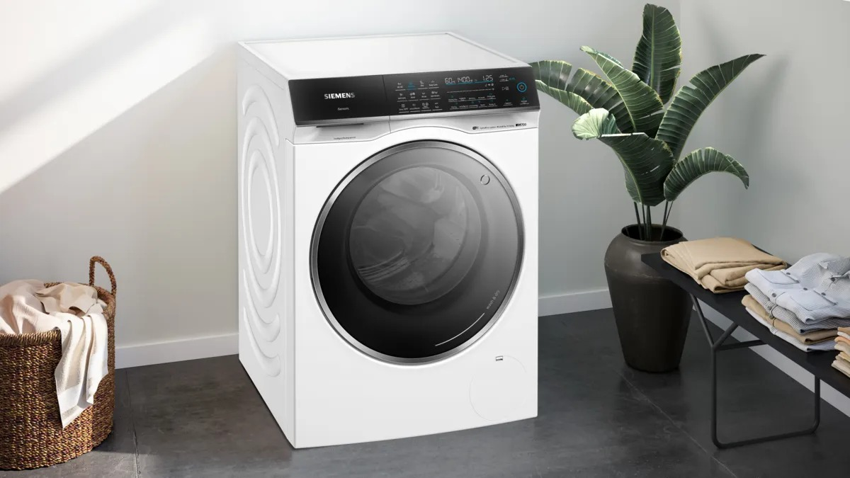 A white Siemens washing machine in a modern room, with laundry basket and plant nearby.