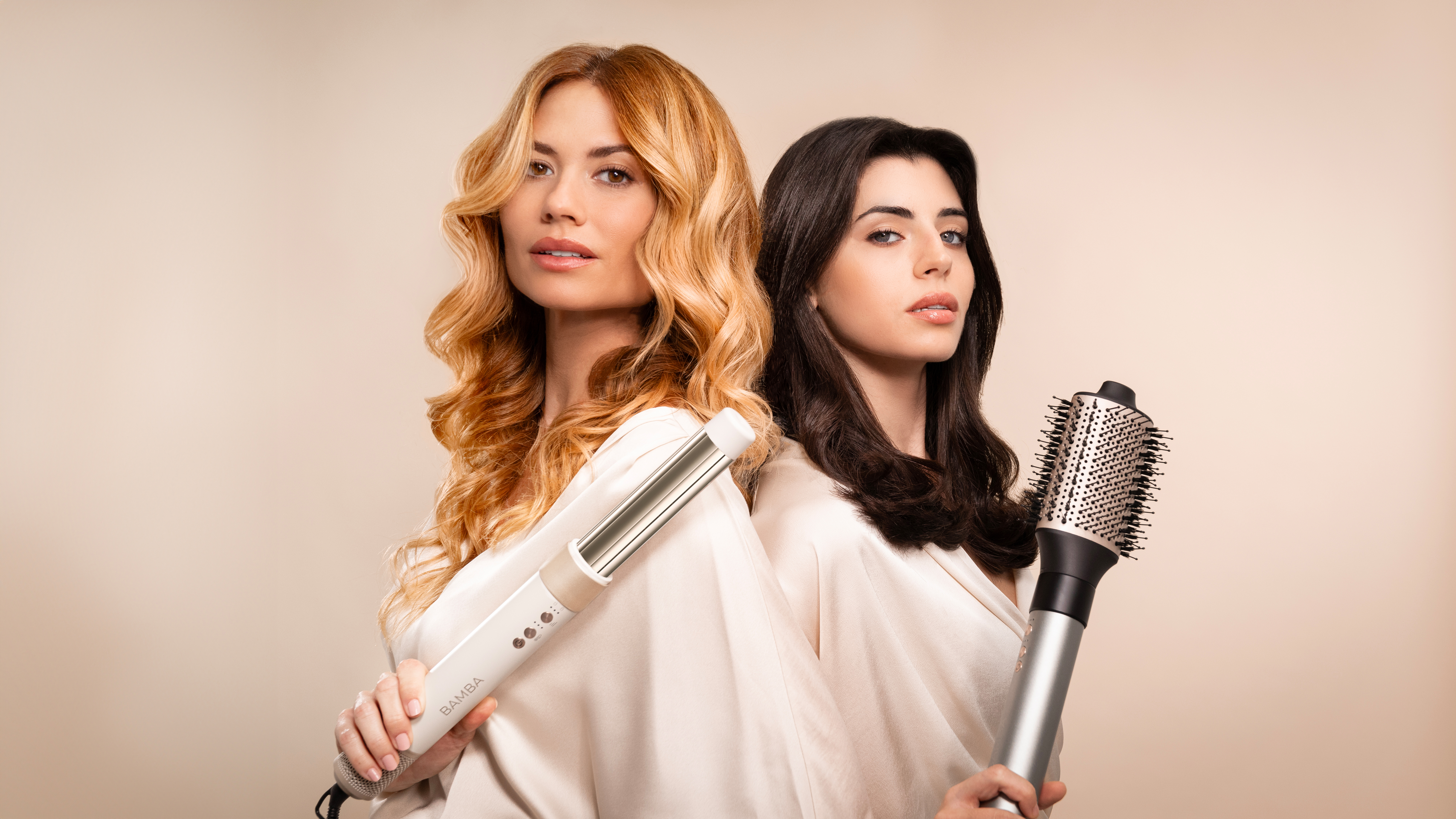 Dos mujeres con cabello rubio y oscuro, sosteniendo herramientas de peinado, mirando a la cámara.