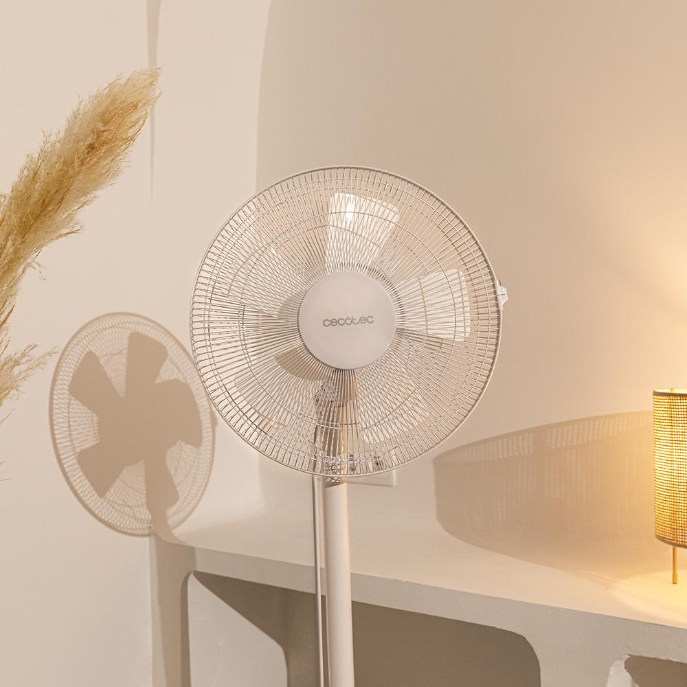 Ventilador de pie blanco con cabezal redondo, aspas visibles, en habitación con lámpara y planta.