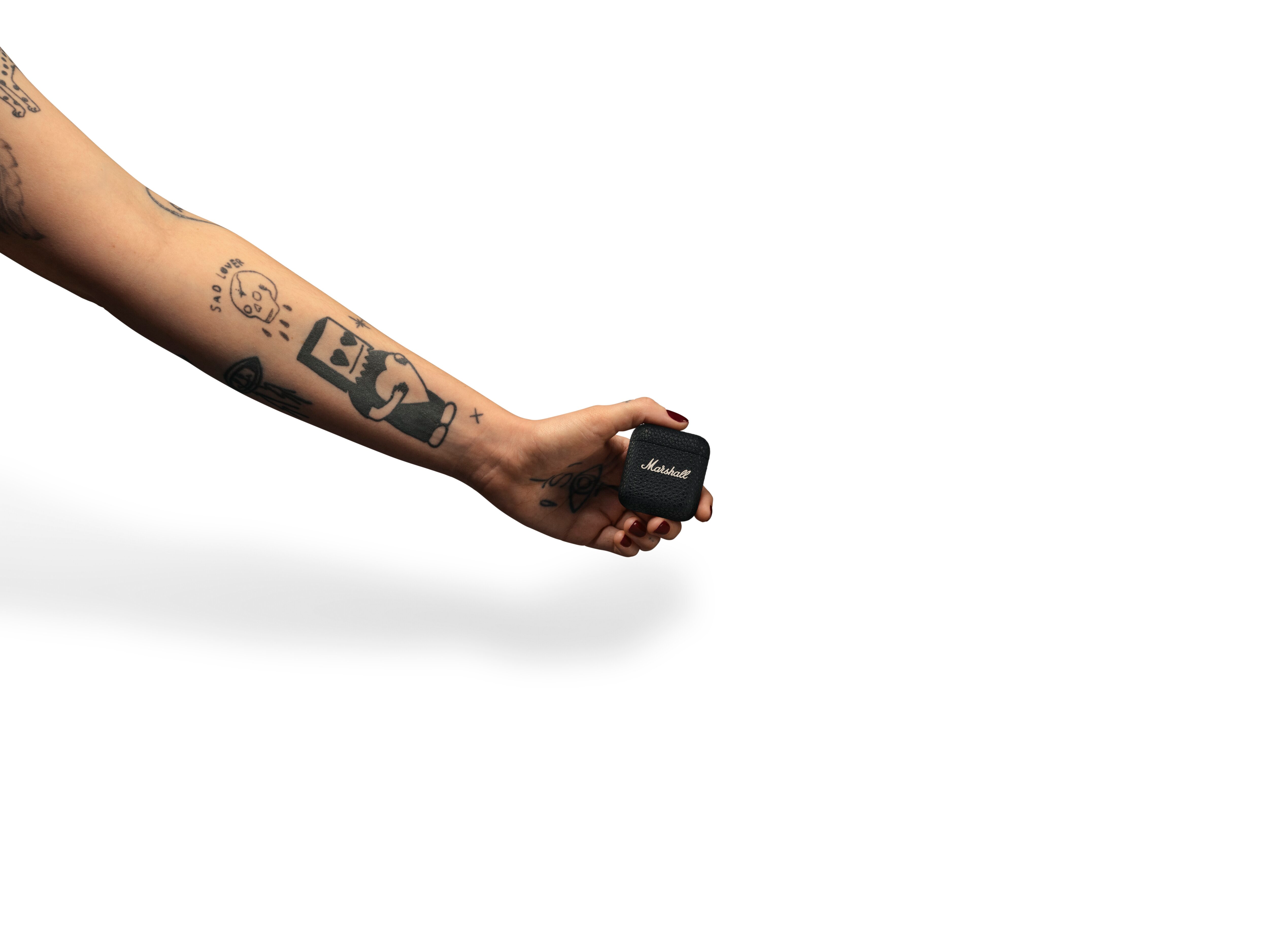 Un braccio tatuato che tiene una custodia nera per auricolari Marshall su bianco.