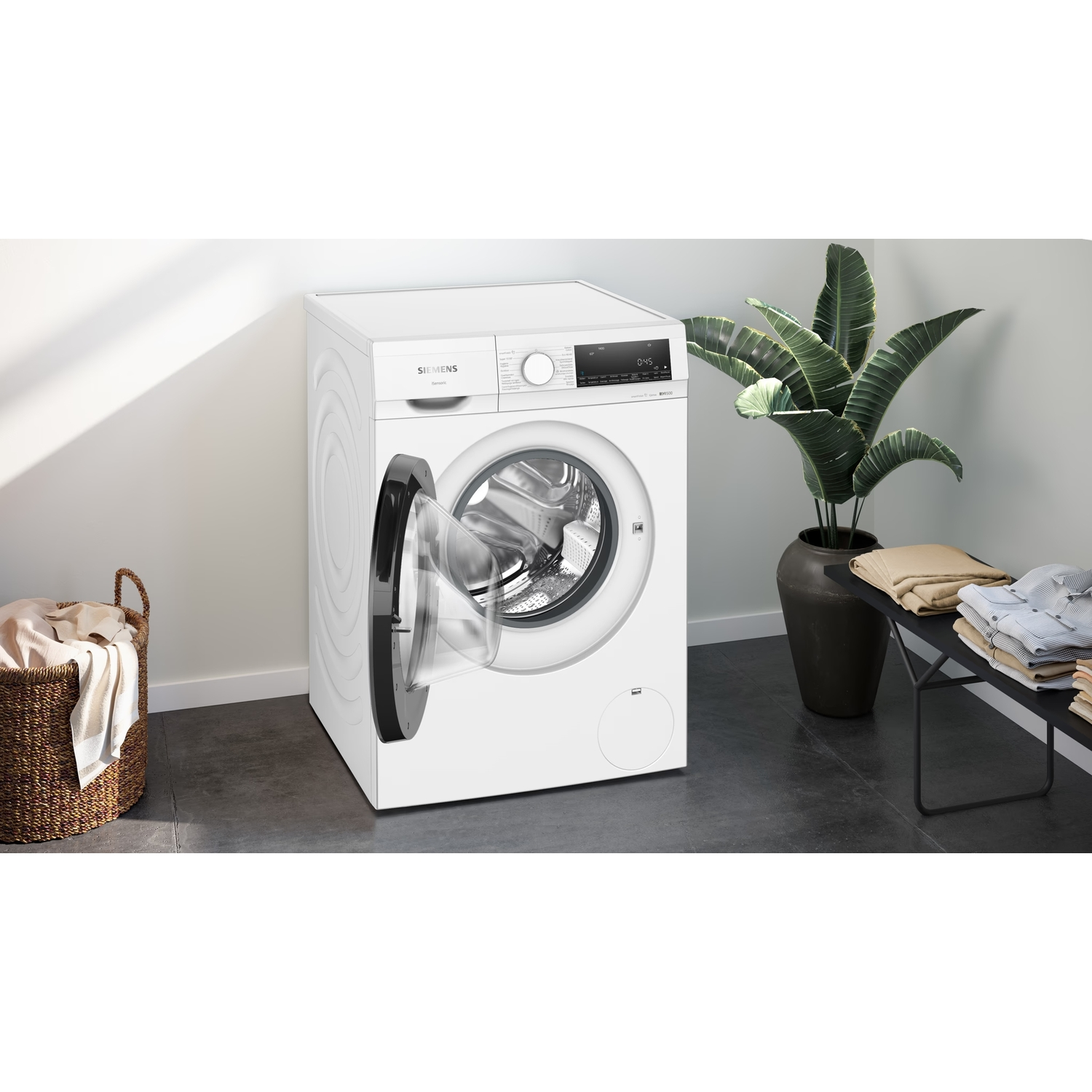 A white Siemens washing machine with the door open. A basket of clothes is on the left. Some clothes are on the right.