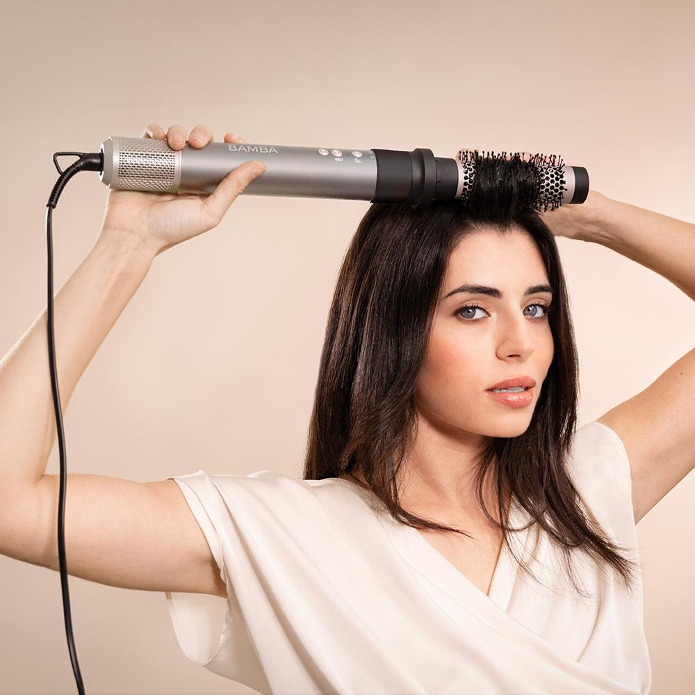 Una mujer peinando su cabello con un moldeador Bamba. Sostiene el moldeador sobre su cabeza.
