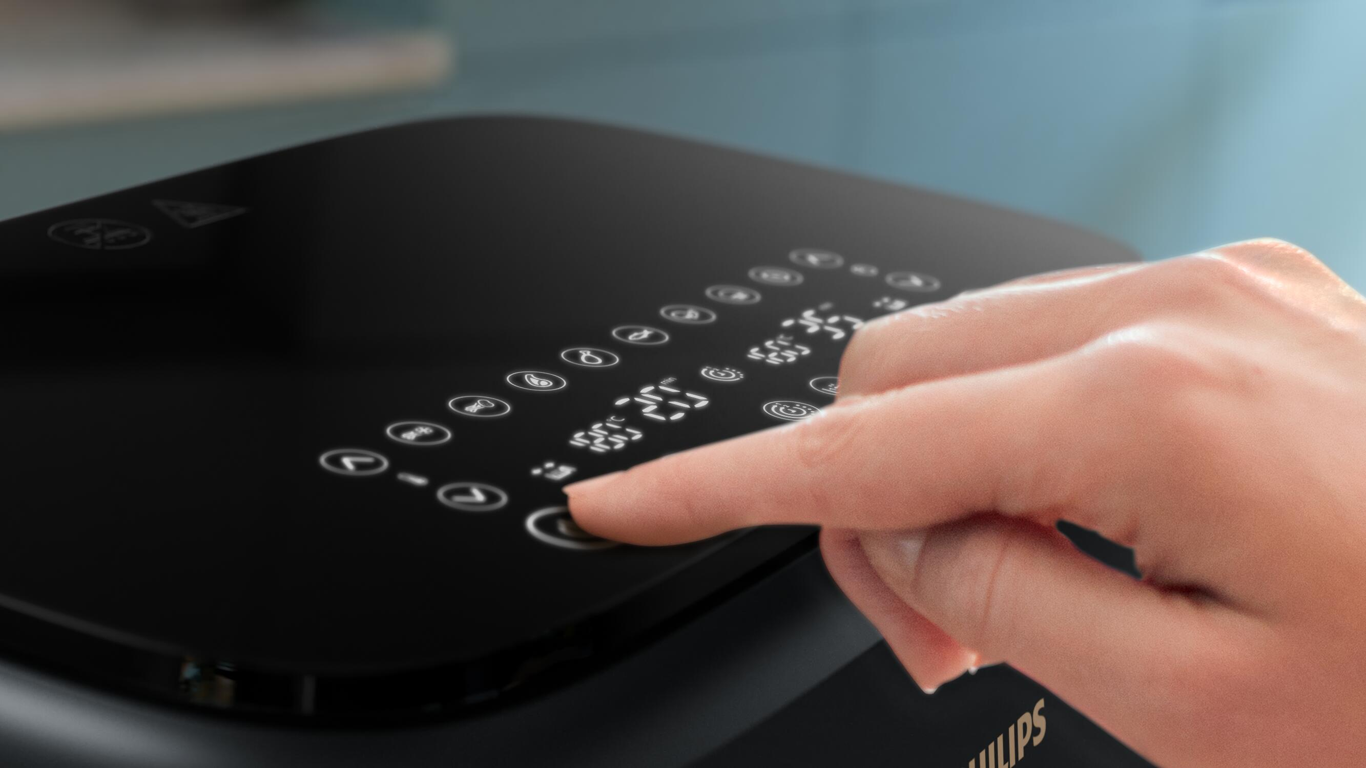 Dłoń naciskająca przycisk na czarnym, dotykowym panelu sterowania urządzenia.