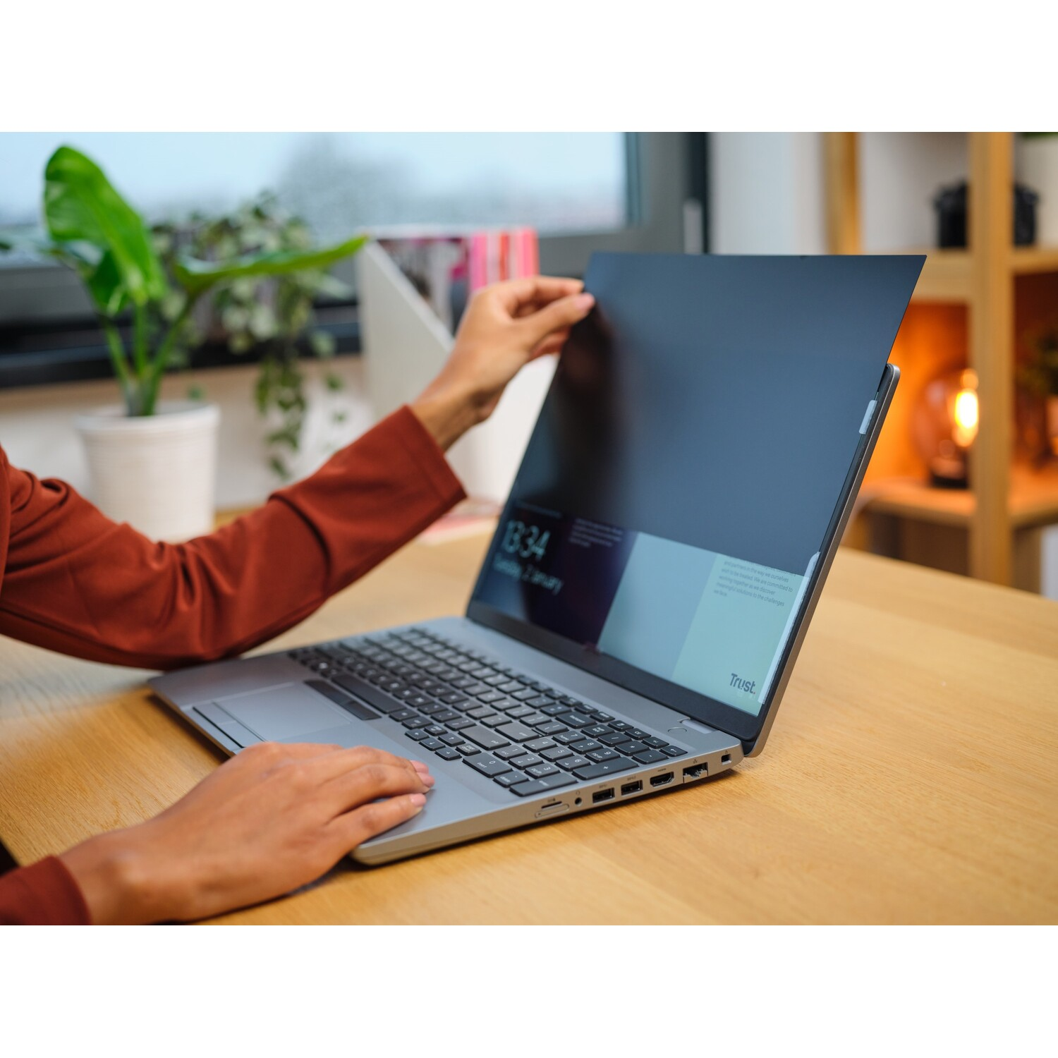 Persoon die een privacy scherm over een laptopscherm houdt. Binnen, op een houten tafel.