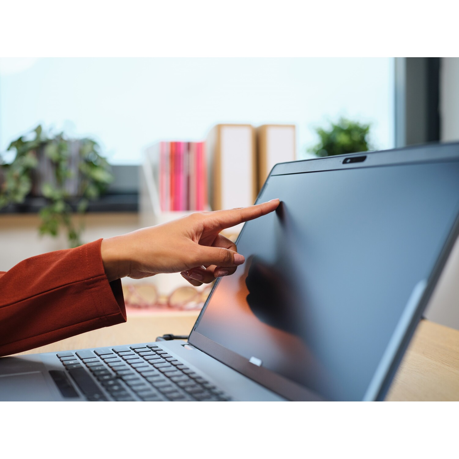 Hand wijst naar laptopscherm. Laptop op houten bureau. Kantooromgeving op de achtergrond.