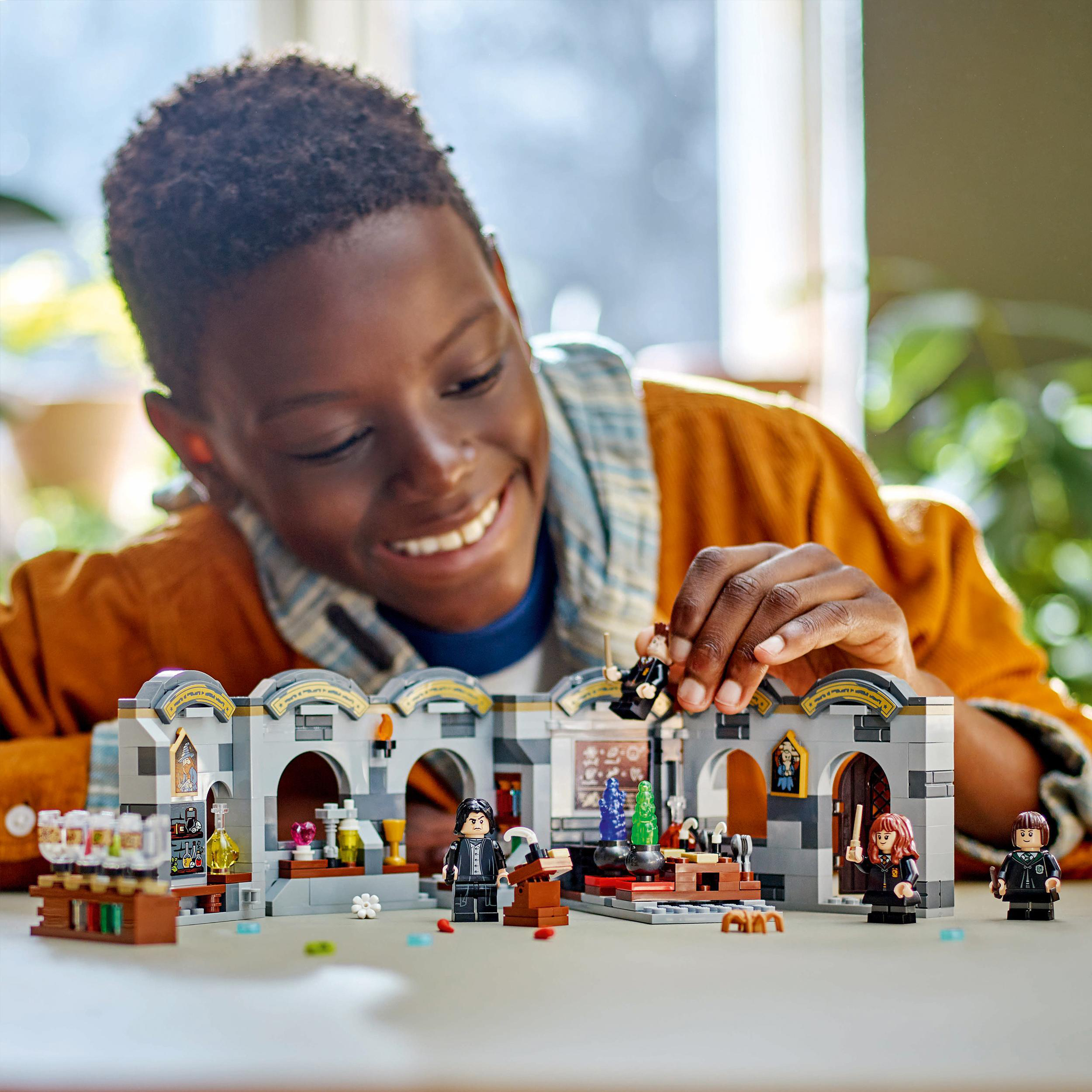 Junge spielt mit einem LEGO-Set und lächelt. Das Set zeigt Figuren und Gebäude aus einer Harry-Potter-Szene.