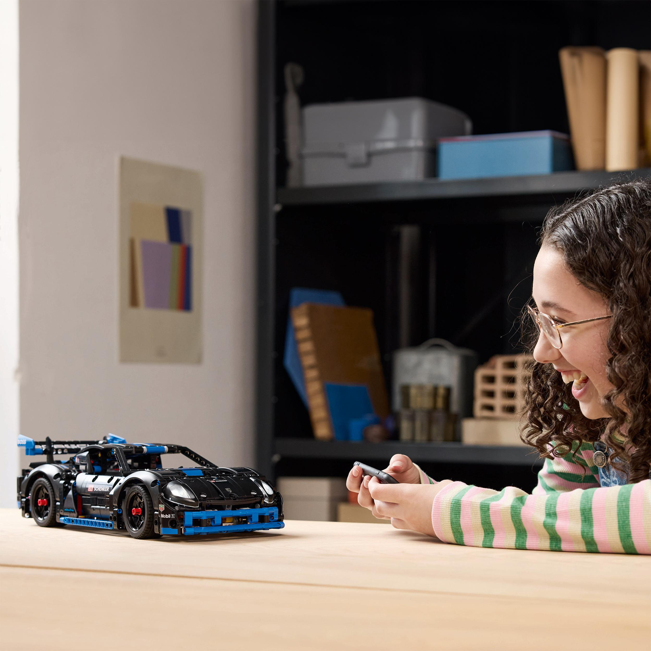 Ein Mädchen lächelt, während es ein schwarzes Spielzeugauto mit einer Fernbedienung steuert.