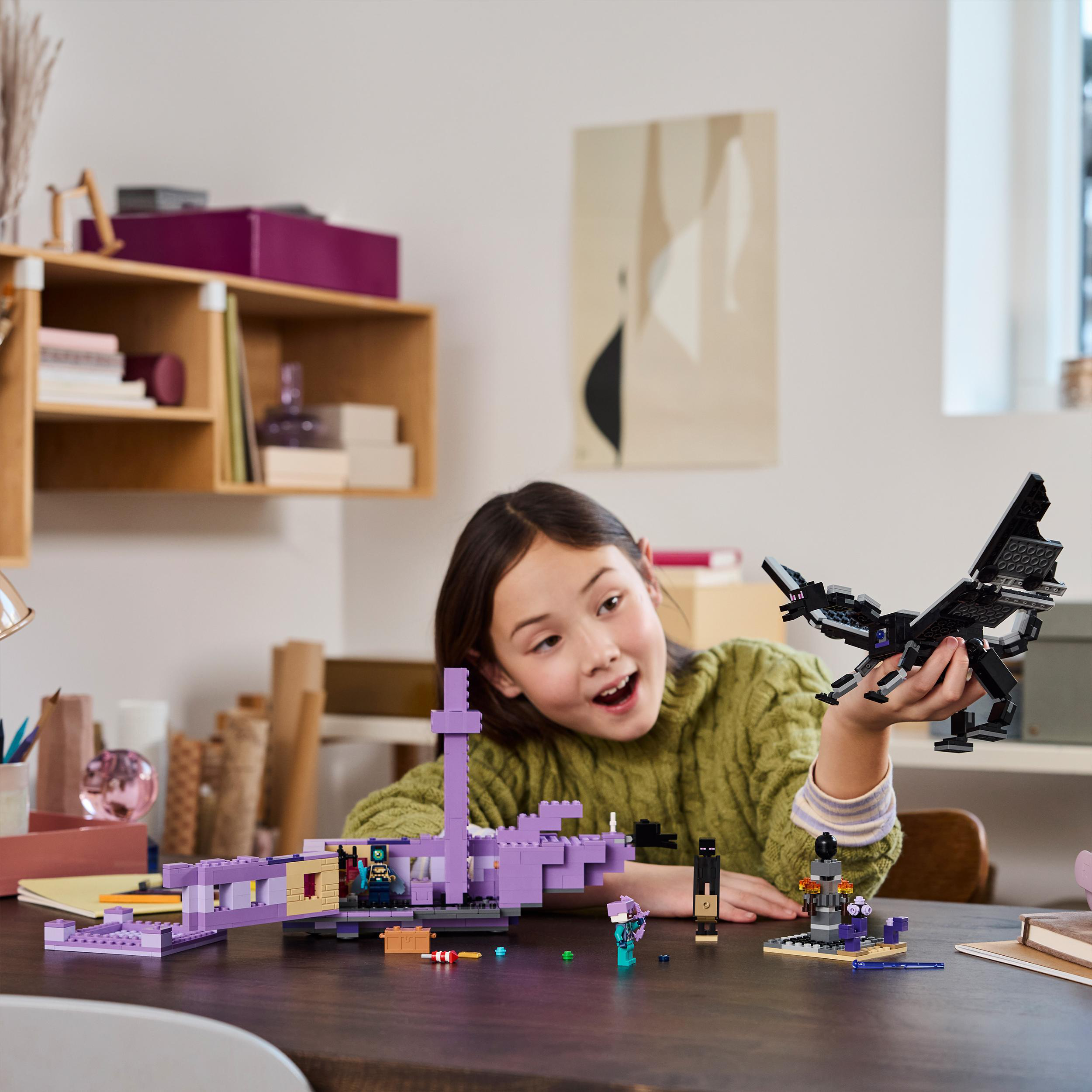 Ein Mädchen spielt mit einem Lego Minecraft Set. Enthält Figuren und Bausteine. Auf einem Tisch.