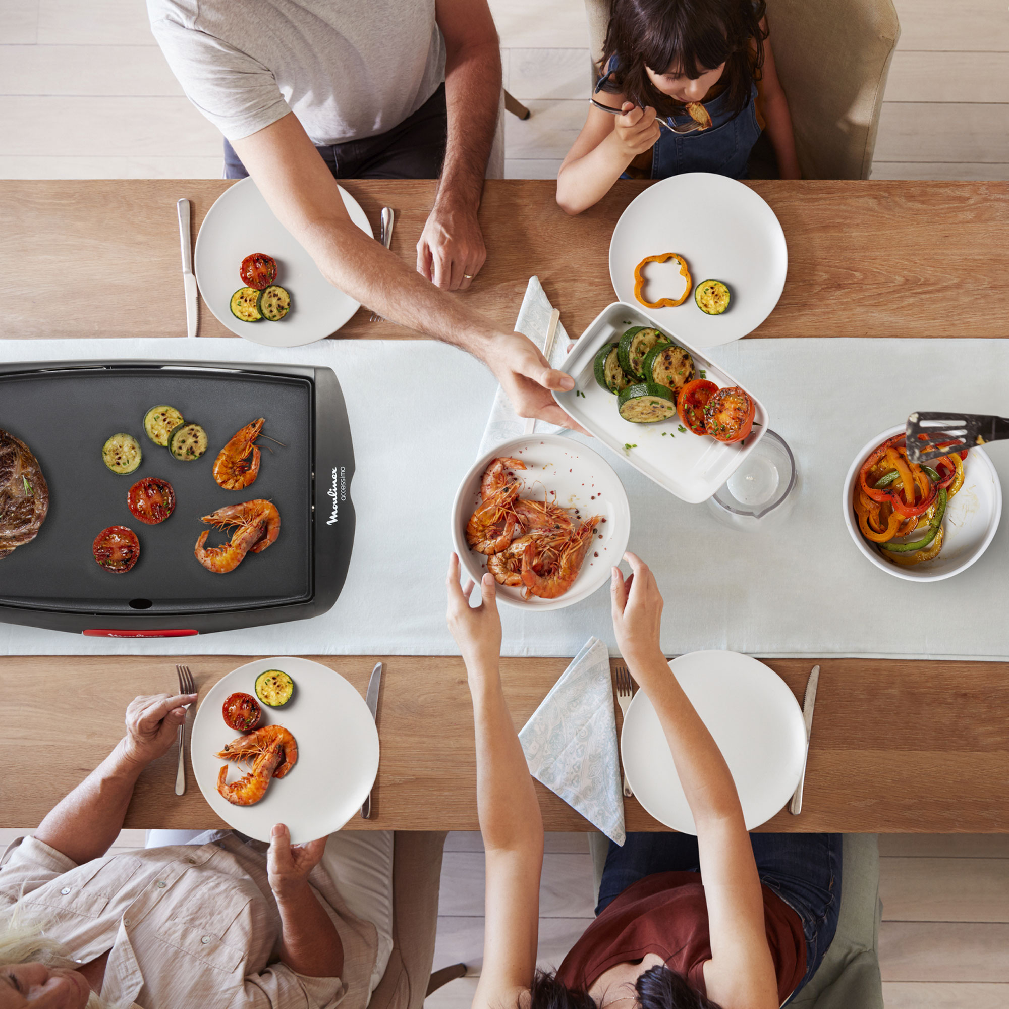Una familia reunida alrededor de una mesa, con una parrilla y comida, incluyendo camarones y verduras.