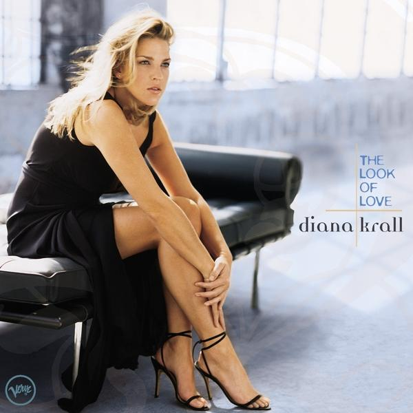 Diana Krall fekete ruhában, egy padon ül. A háttér kék színátmenetes.