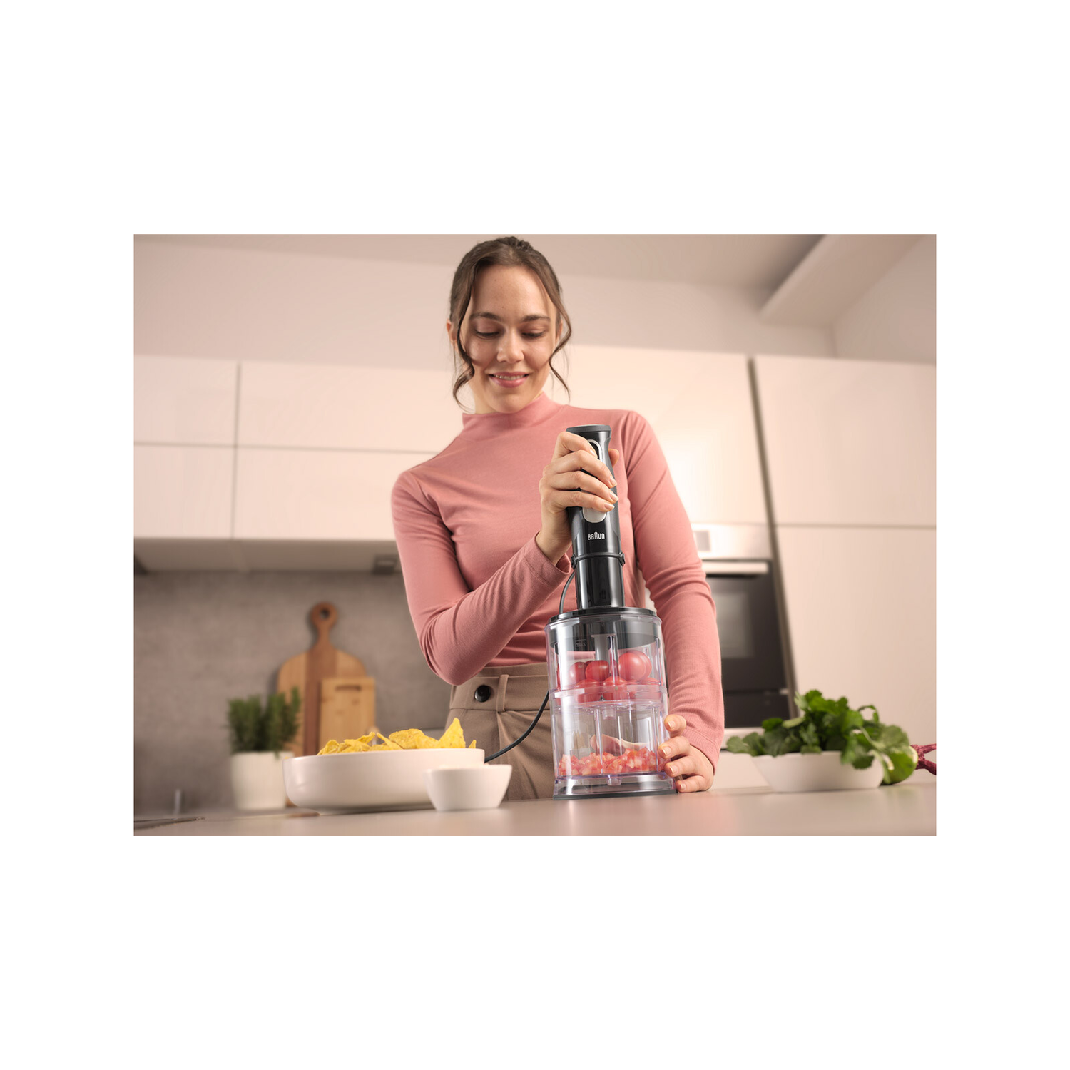 Vrouw die een zwarte Braun staafmixer gebruikt met ingrediënten.