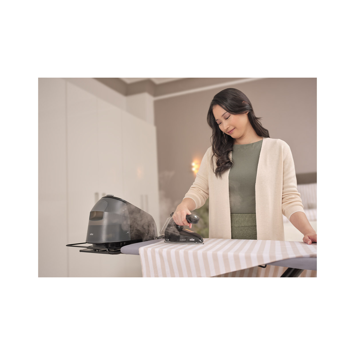 Woman ironing a striped fabric on a white ironing board, grey iron, steam. Background: room.
