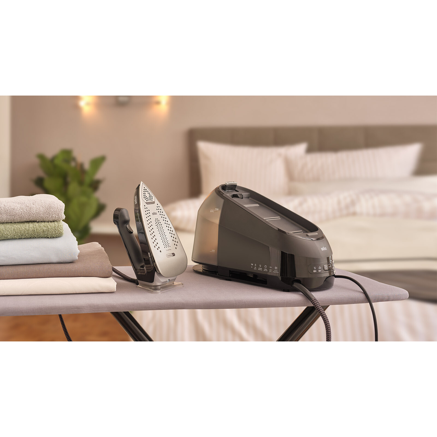Ironing station with iron and steam generator, towels, and a bed in the background.