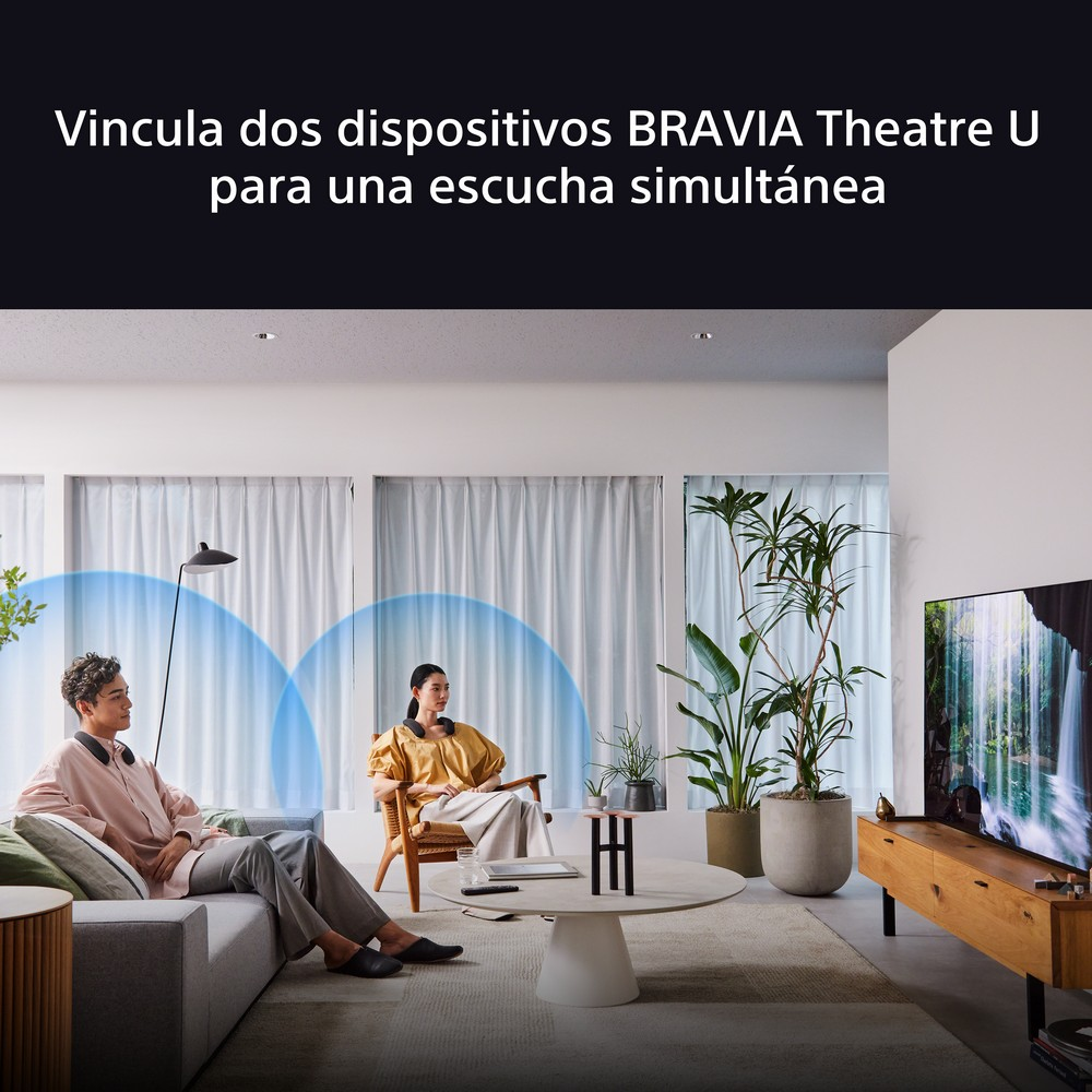 Dos personas escuchando auriculares en salón, con TV y plantas al fondo.