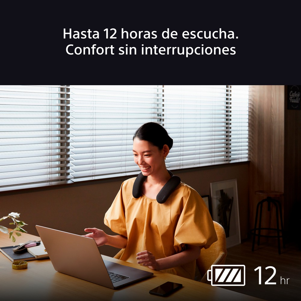 Mujer usando una laptop, usando un altavoz de cuello. Sonríe en una habitación bien iluminada.