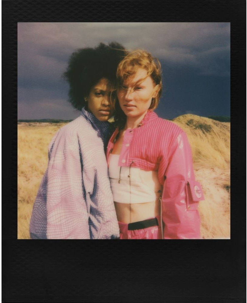 Photo Polaroid de deux femmes. Une avec une veste rose, l'autre avec une veste bleue.