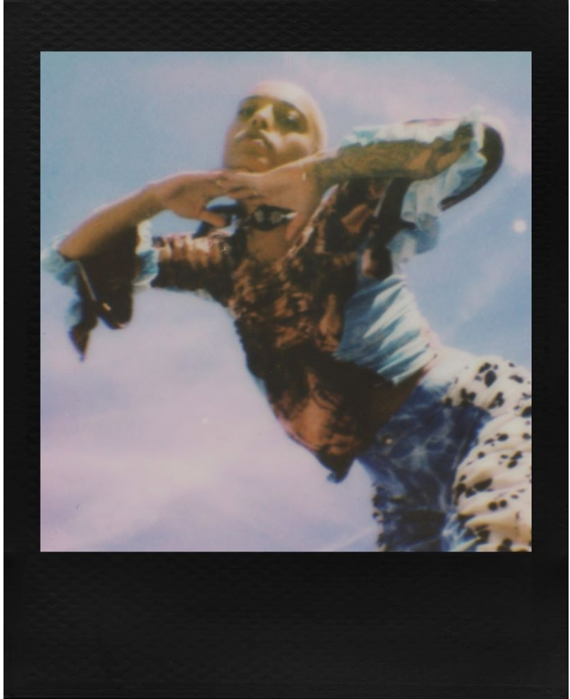 Une personne dans une tenue colorée, capturée dans une photo Polaroid vintage contre un ciel bleu.