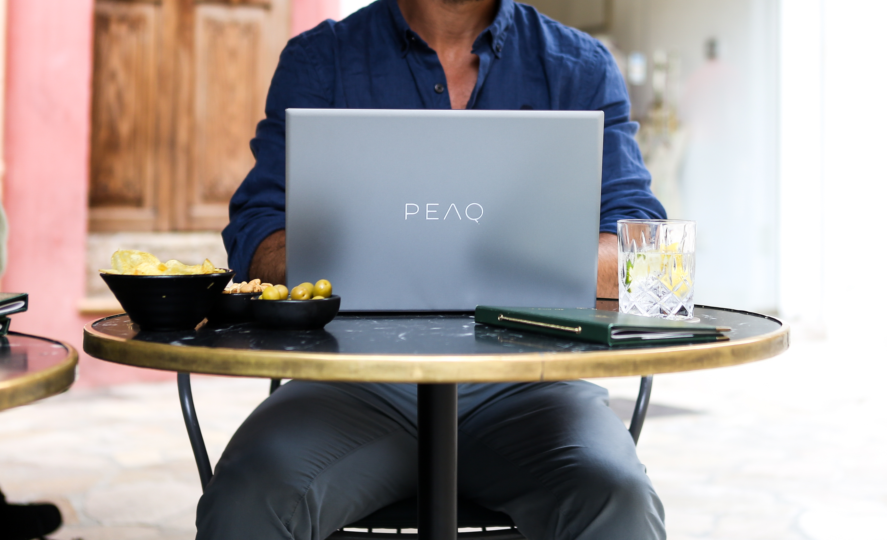 Eine Person arbeitet an einem Laptop an einem Tisch mit Snacks und einem Getränk, im Freien in einem Café.