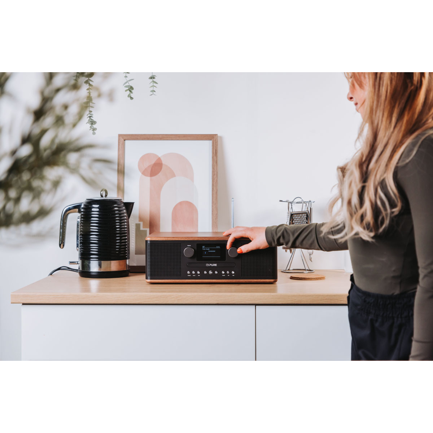 A woman turns a knob on a radio placed on a counter.