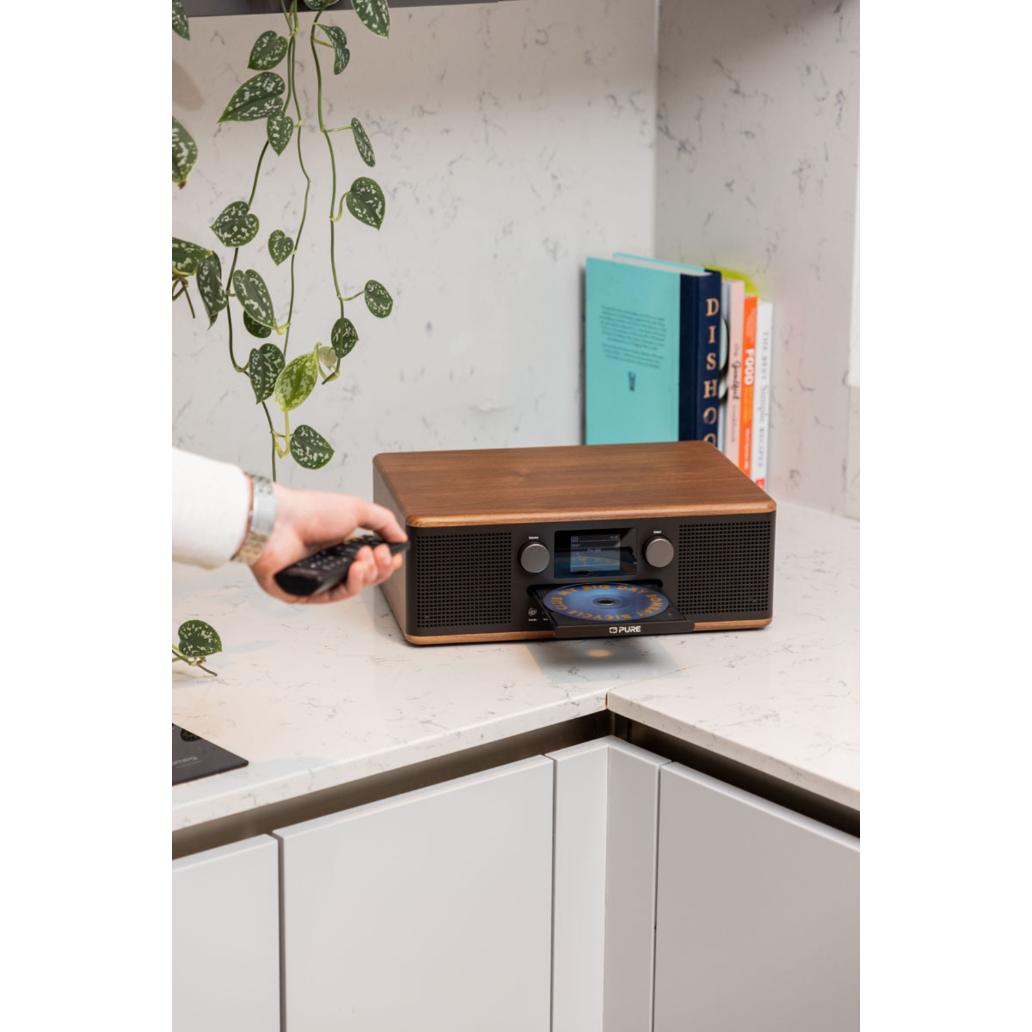 A CD player with a wooden top and a remote control, on a kitchen counter.