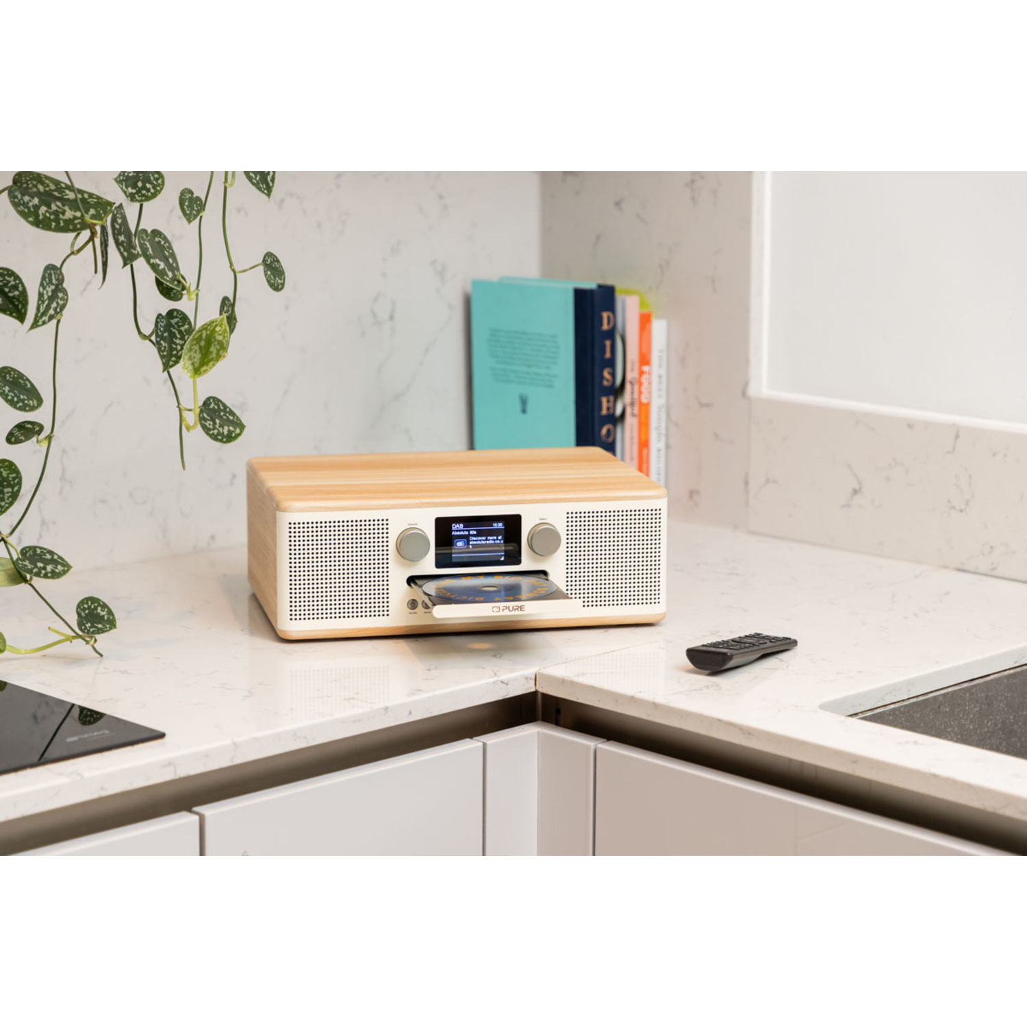 Een witte radio met een cd-sleuf op een aanrecht, met een afstandsbediening.
