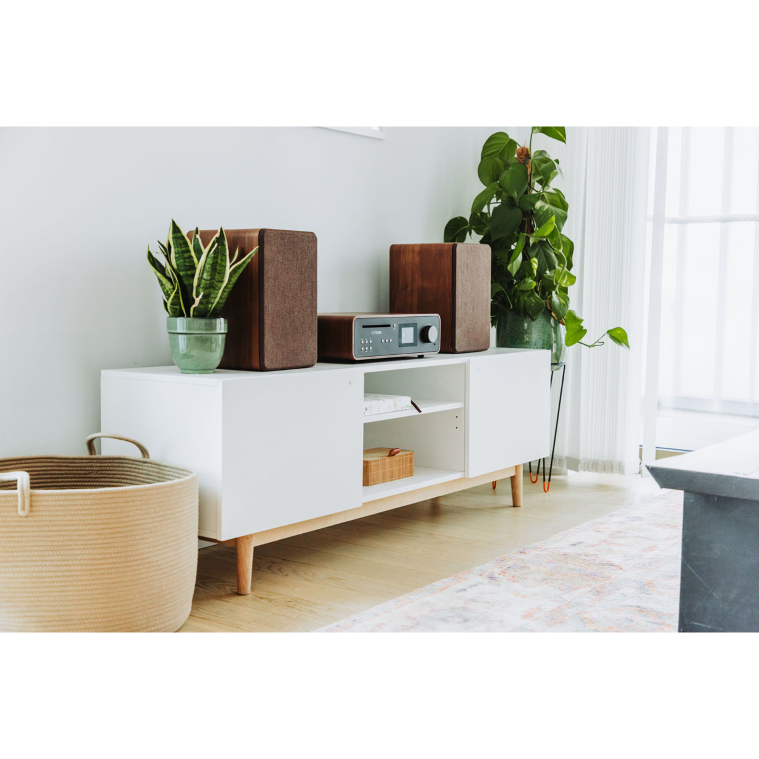 A white cabinet with plants on top, a stereo, and a basket in front, all in a living room.