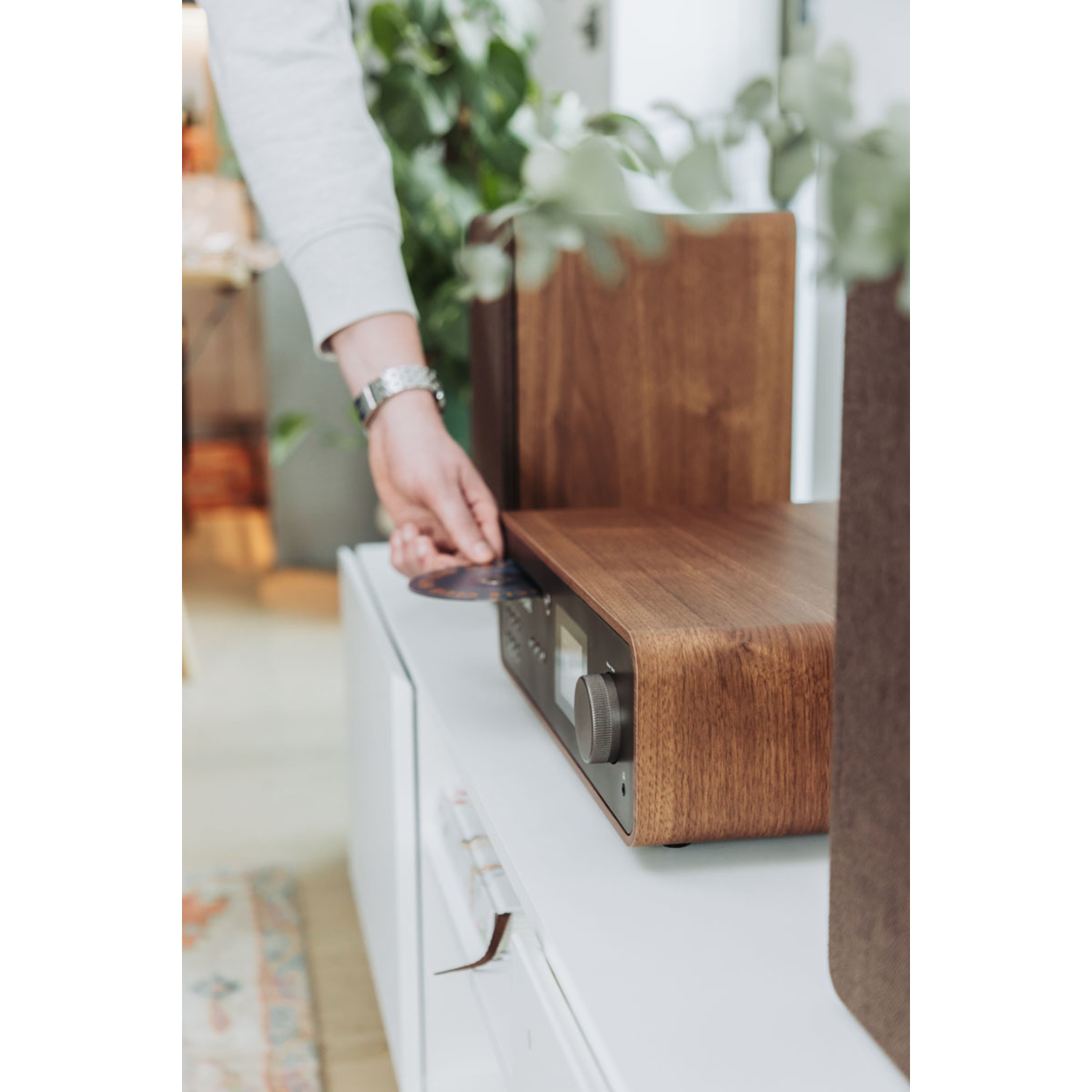 A person inserting a CD into a wooden radio on a white surface.