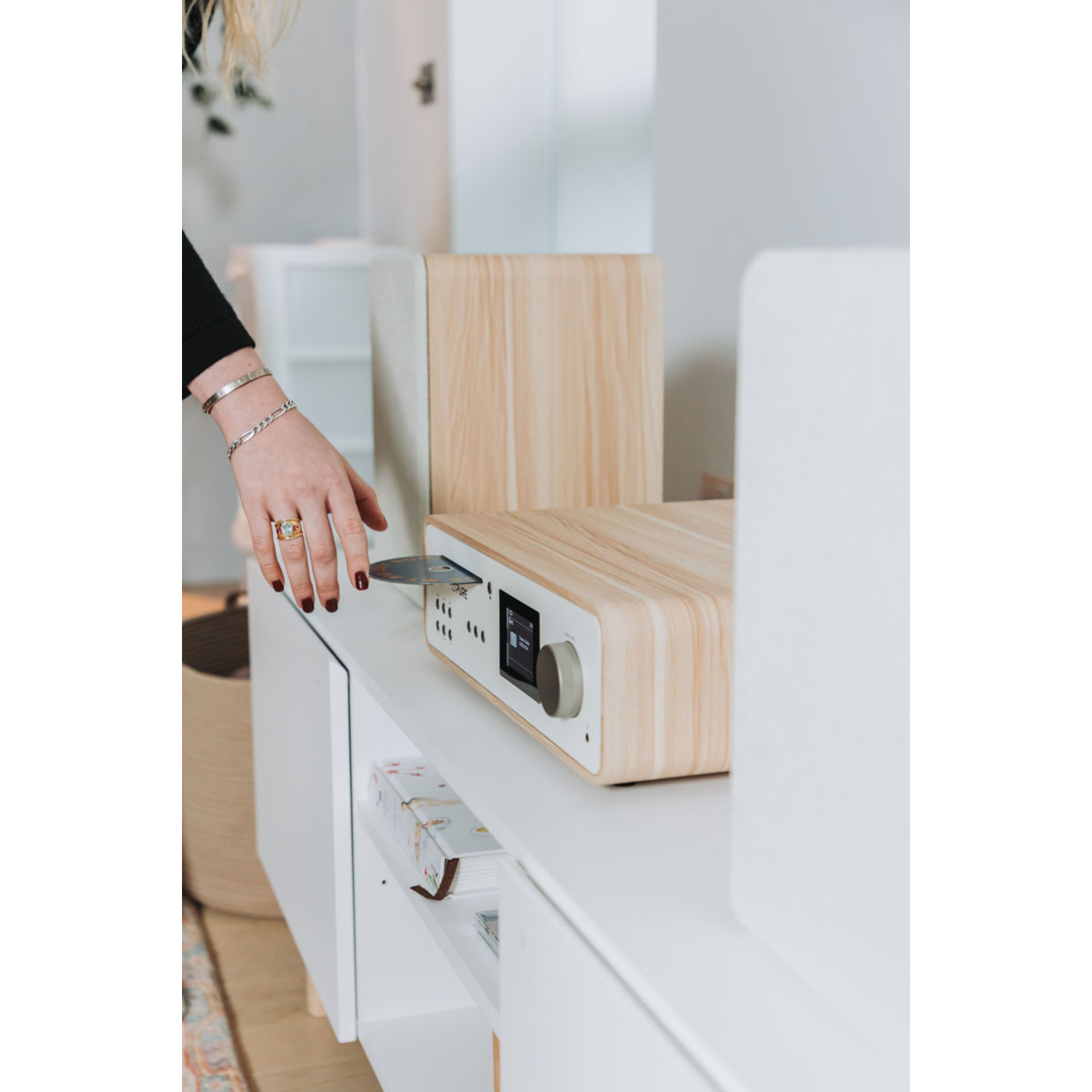 A person's hand is inserting a CD into a white and wooden radio.