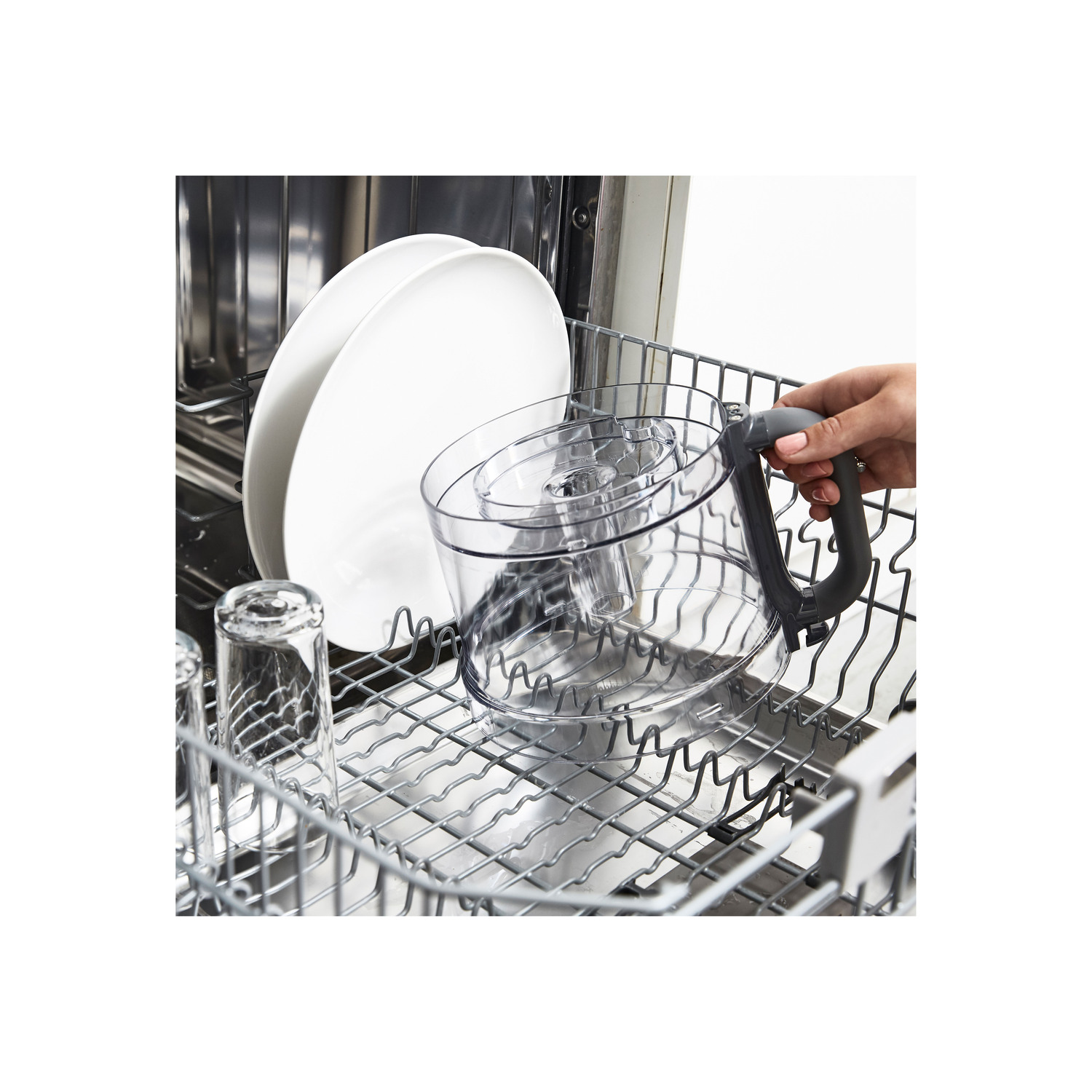 A woman's hand putting a clear plastic food processor part into a dishwasher rack.