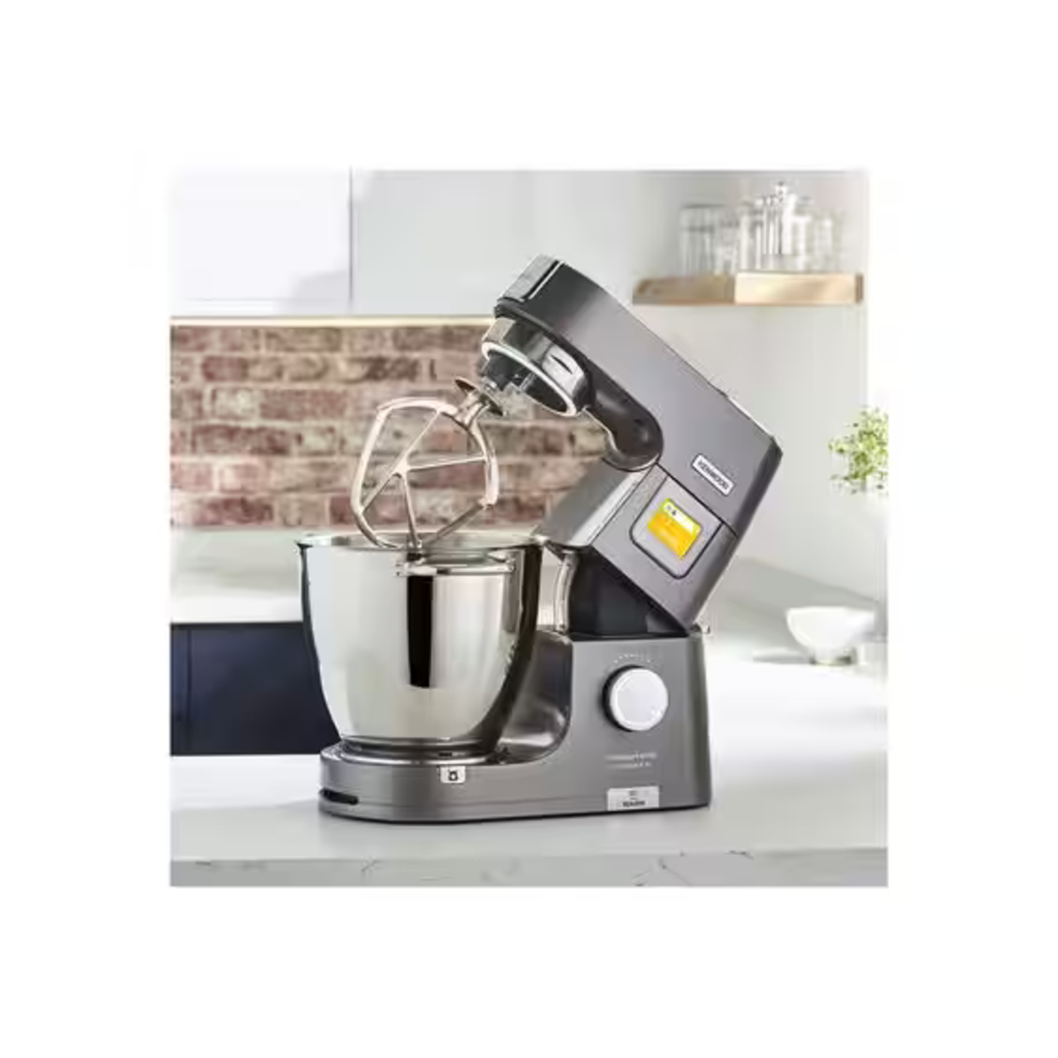 Robot culinaire Kenwood argenté. Bol et accessoire fouet visibles. Arrière-plan de cuisine.