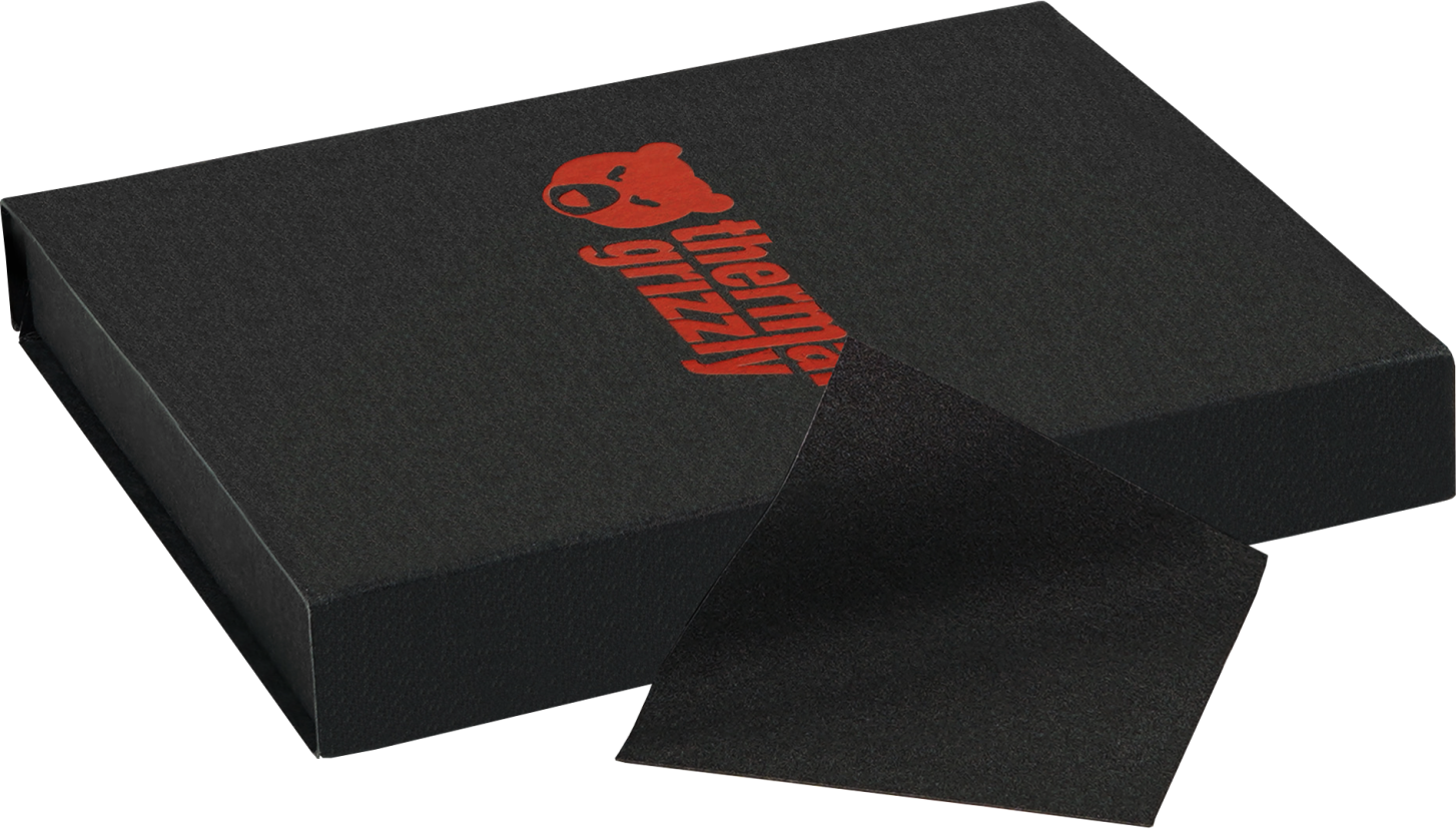 Schwarze Box mit rotem 'thermal grizzly' Text. Ein schwarzes quadratisches Pad liegt daneben.