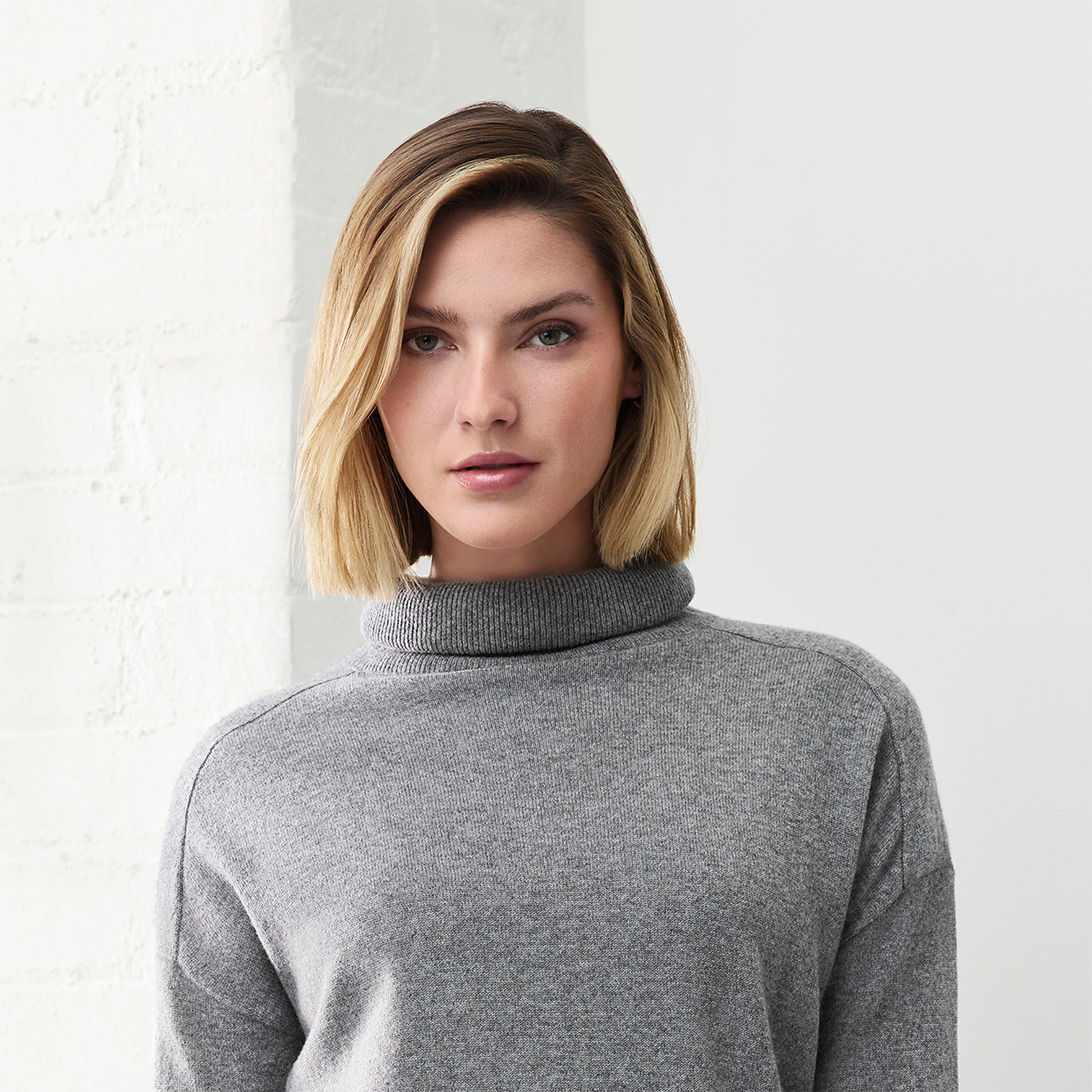 Una donna con i capelli biondi, che indossa un maglione a collo alto grigio e guarda direttamente la fotocamera.