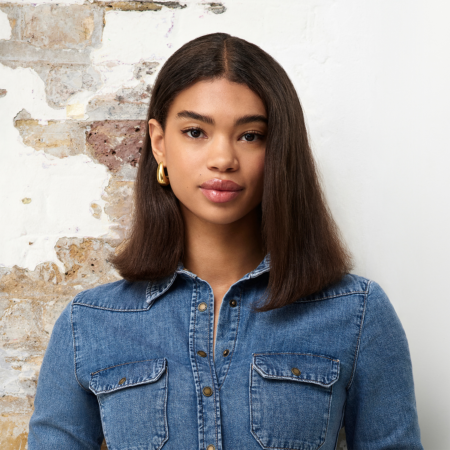Giovane donna con capelli scuri, camicia di jeans e orecchini d'oro.