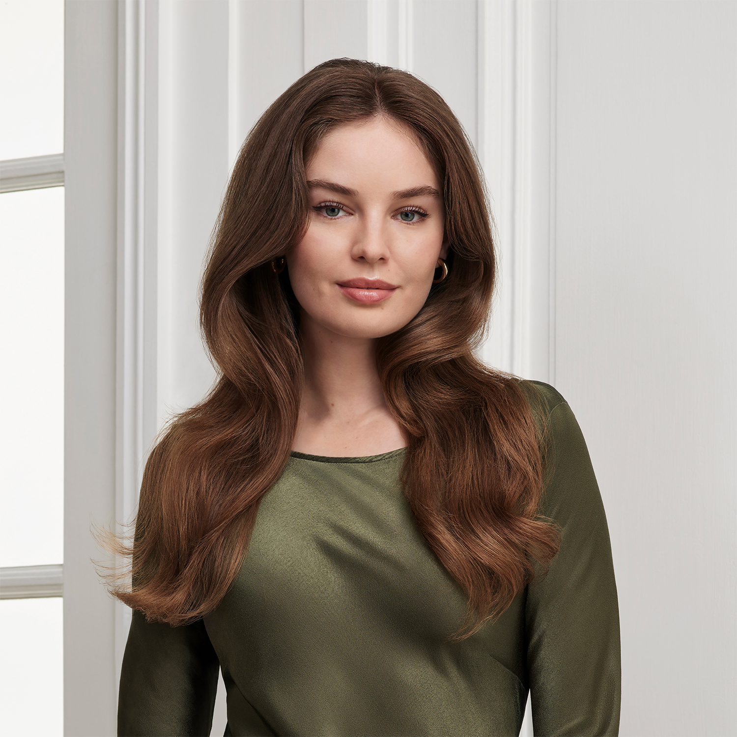 Donna con lunghi capelli castani e top verde. Sfondo bianco.