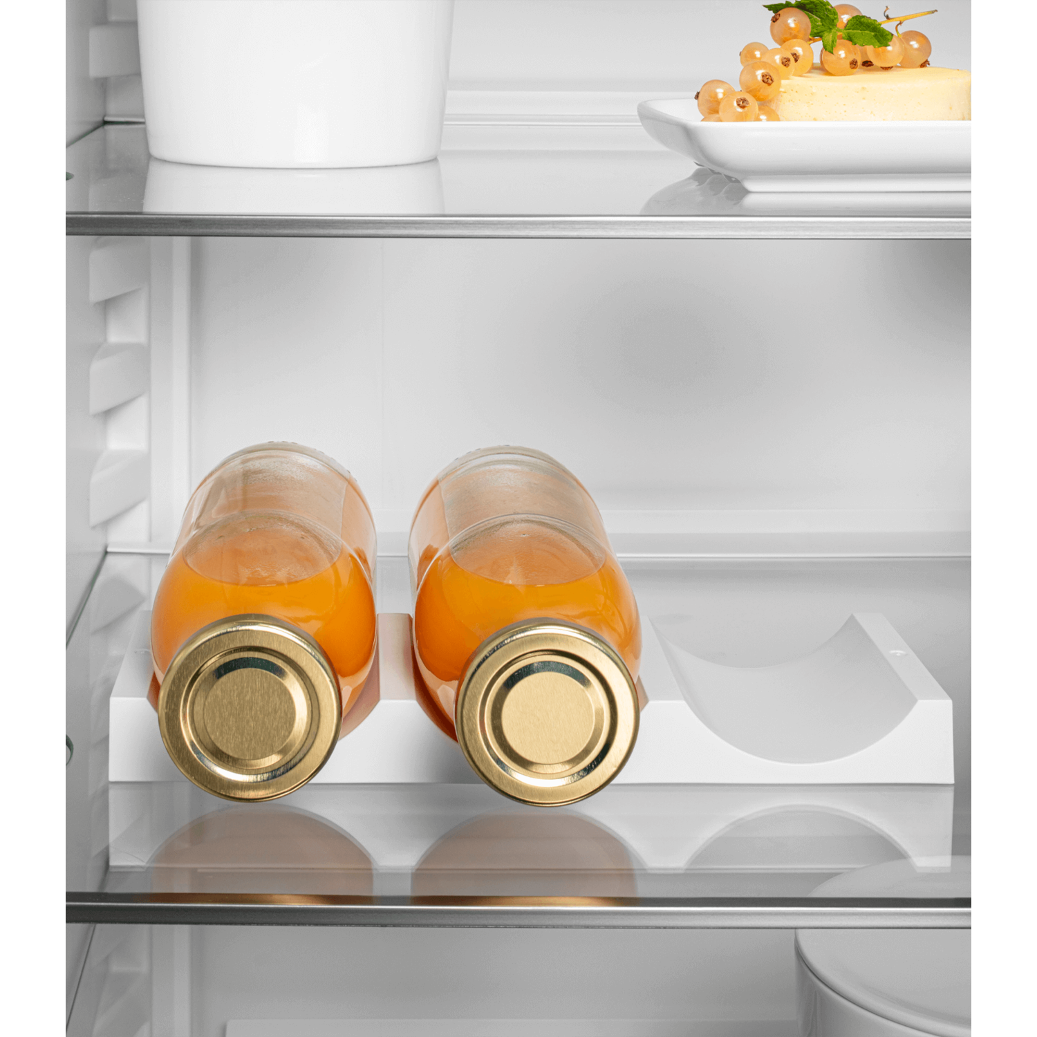 Two bottles of orange juice inside a refrigerator, on a white shelf.