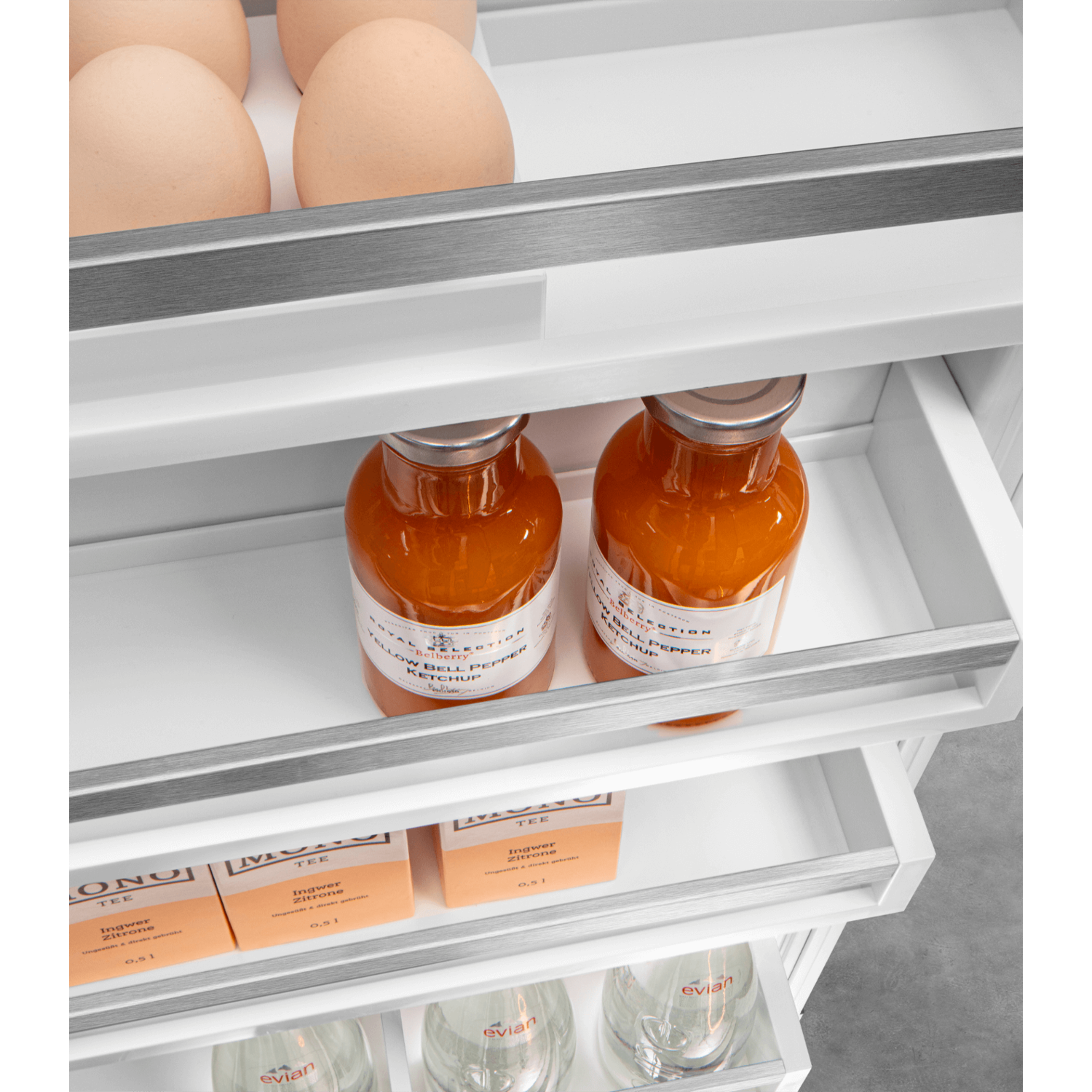 Refrigerator interior with eggs, orange juice bottles, and boxes of lemon tea.