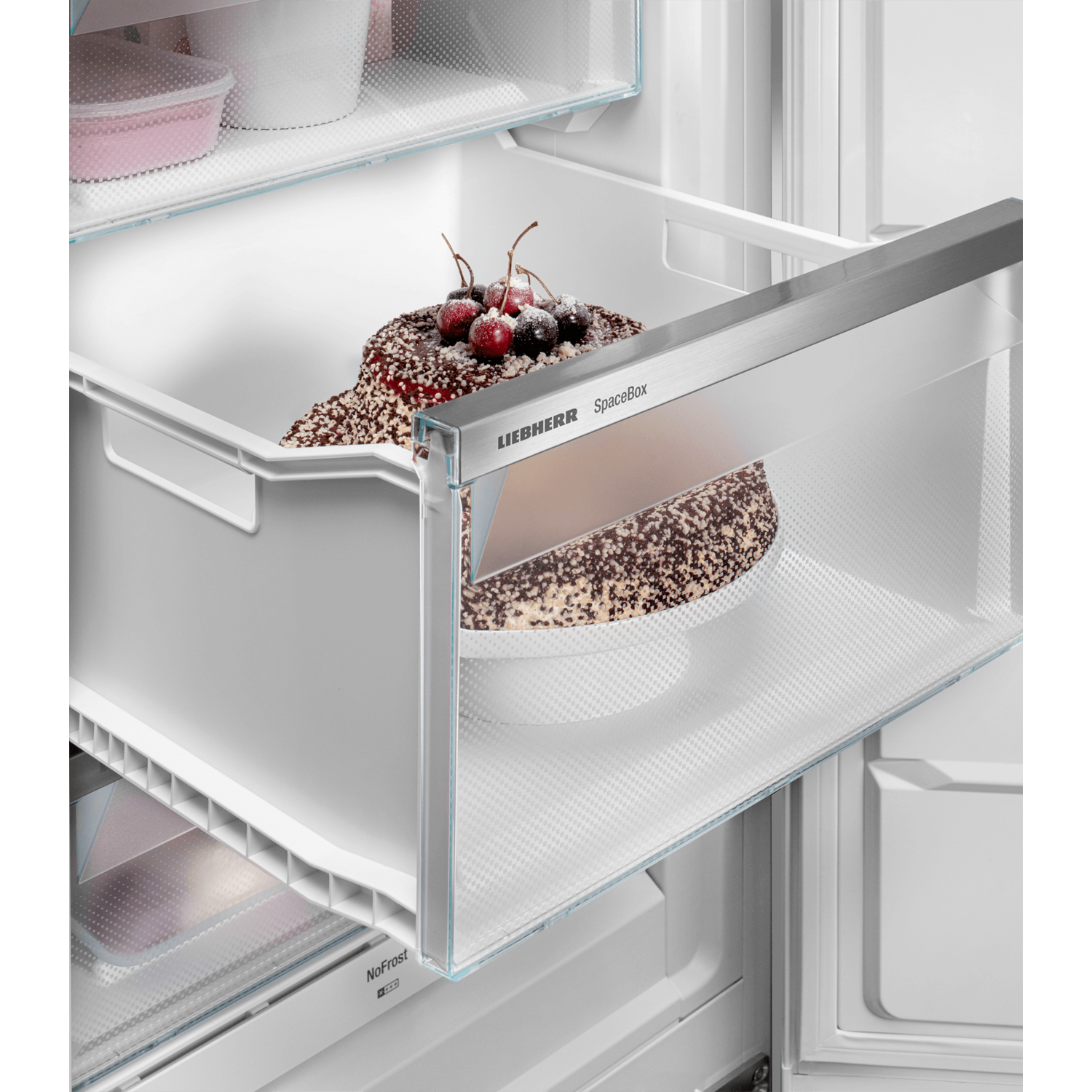 Cake in a refrigerator drawer. The cake has chocolate, nuts and cherries. The drawer is clear.
